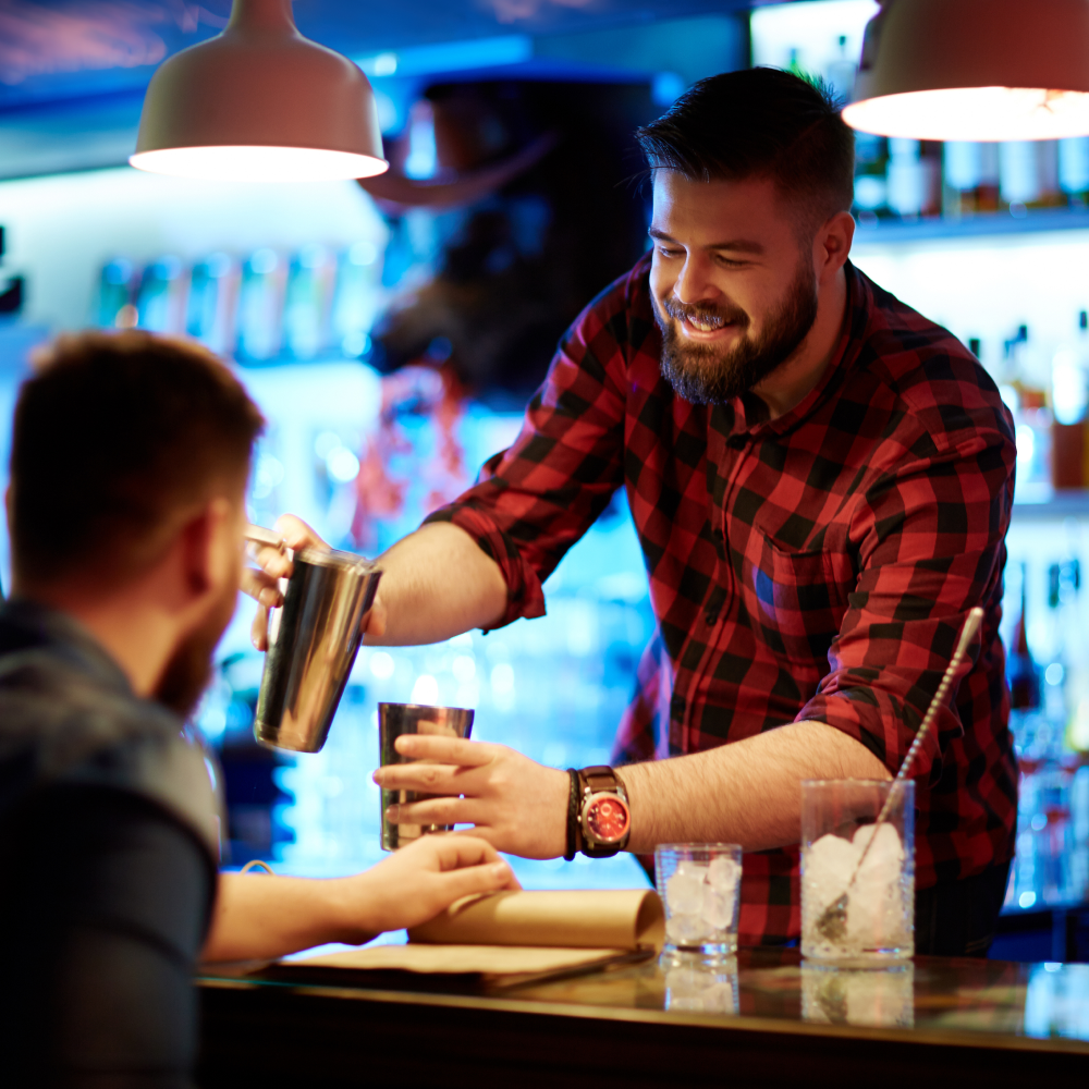 A man is pouring a drink into a glass at a bar.