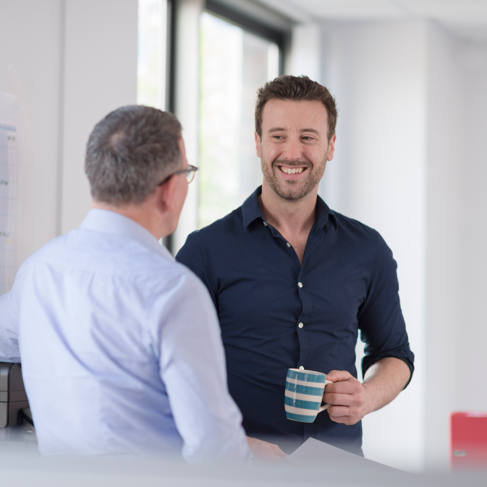 Two men are having a conversation and one is holding a cup of coffee