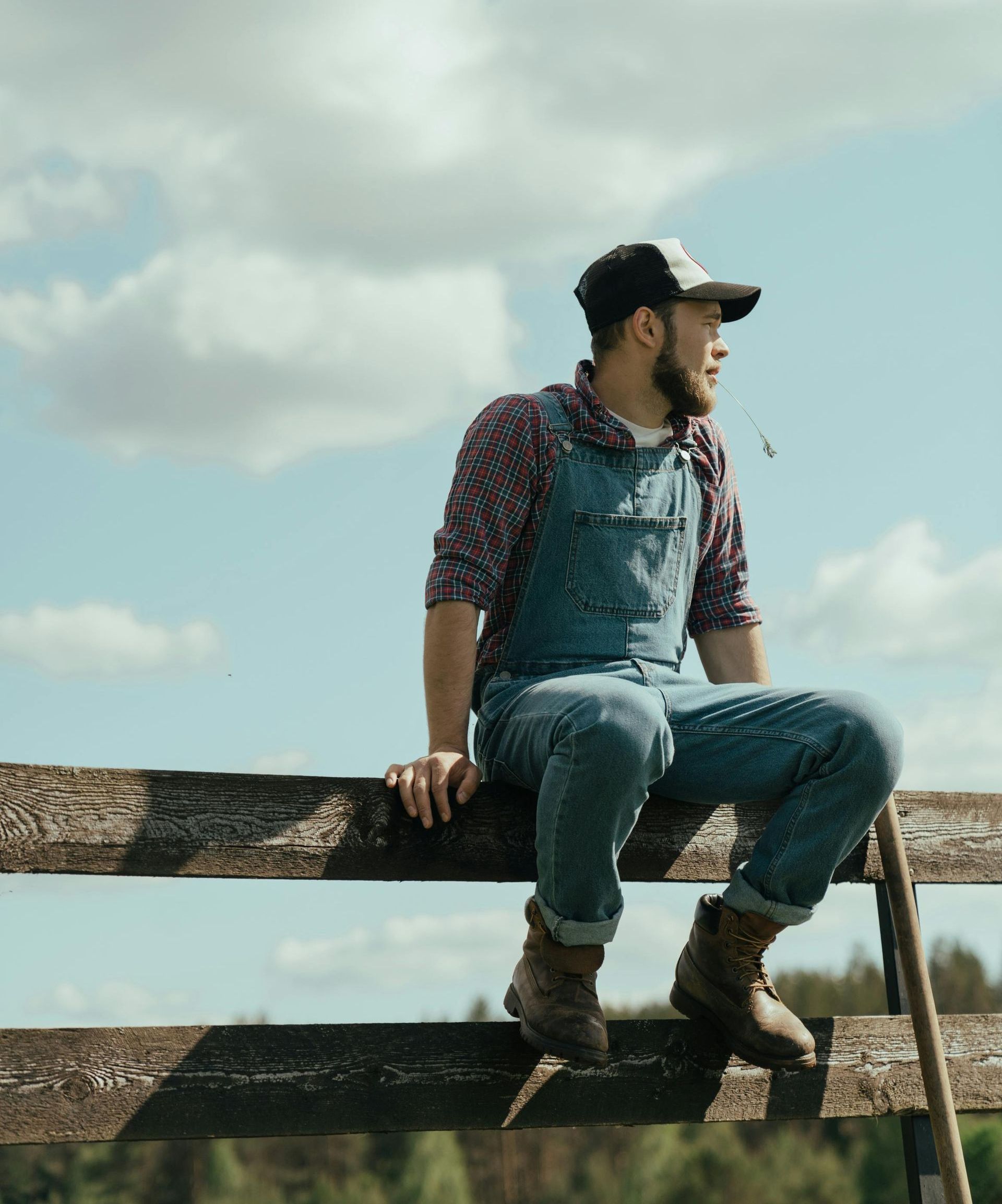 A man in overalls is sitting on a wooden fence.