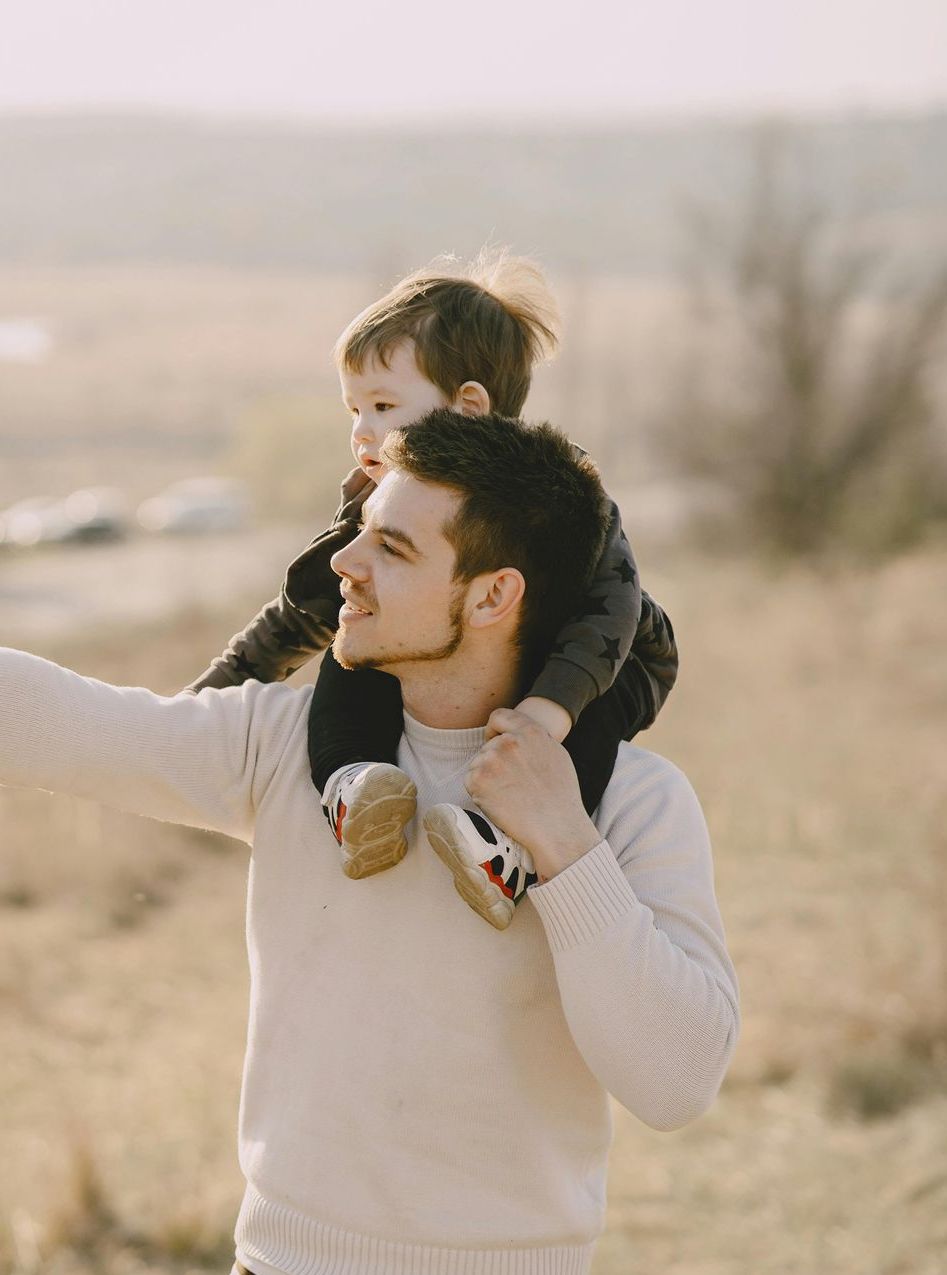 A man is carrying a baby on his shoulders in a field.