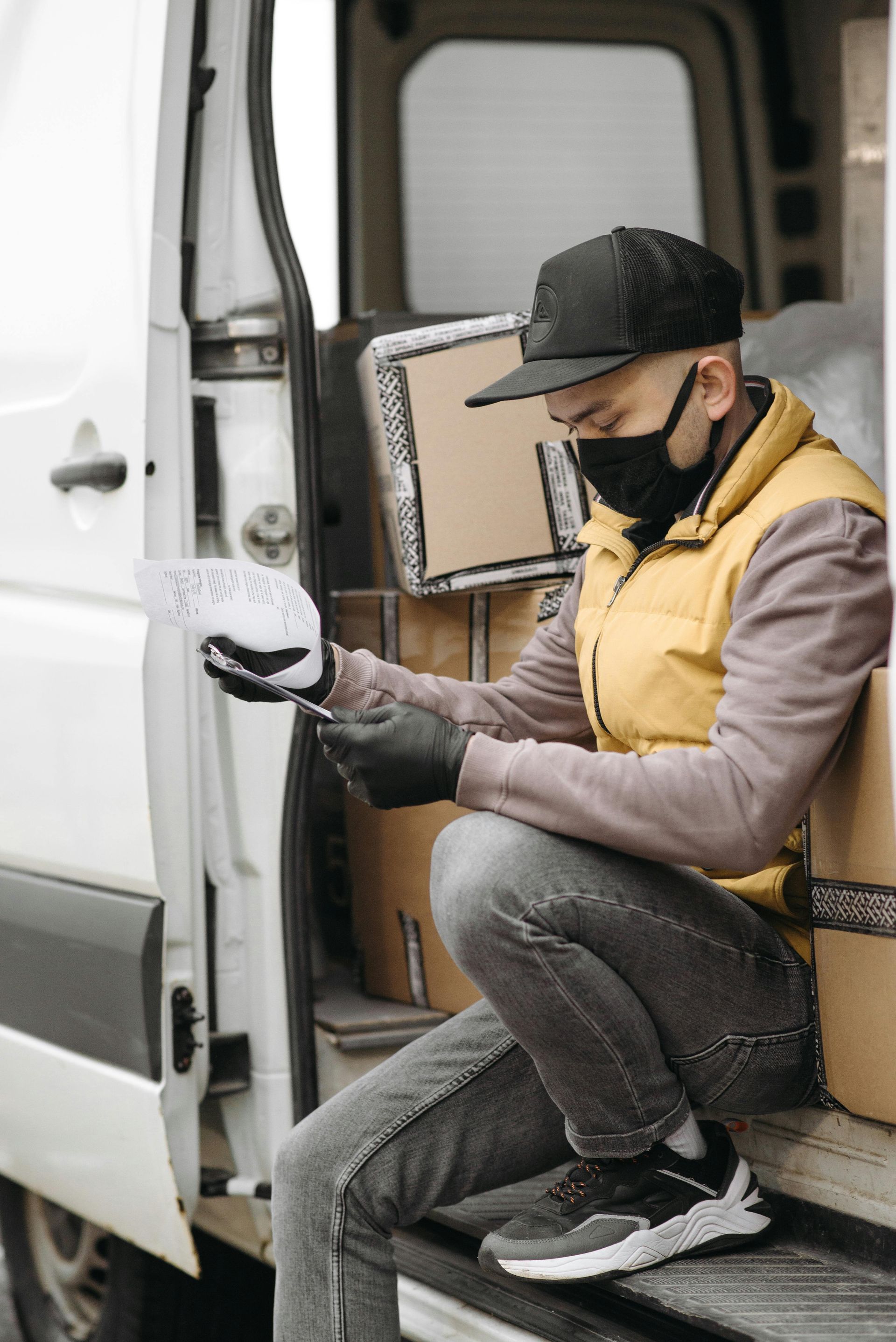 A delivery man wearing a mask and gloves is sitting in the back of a van.