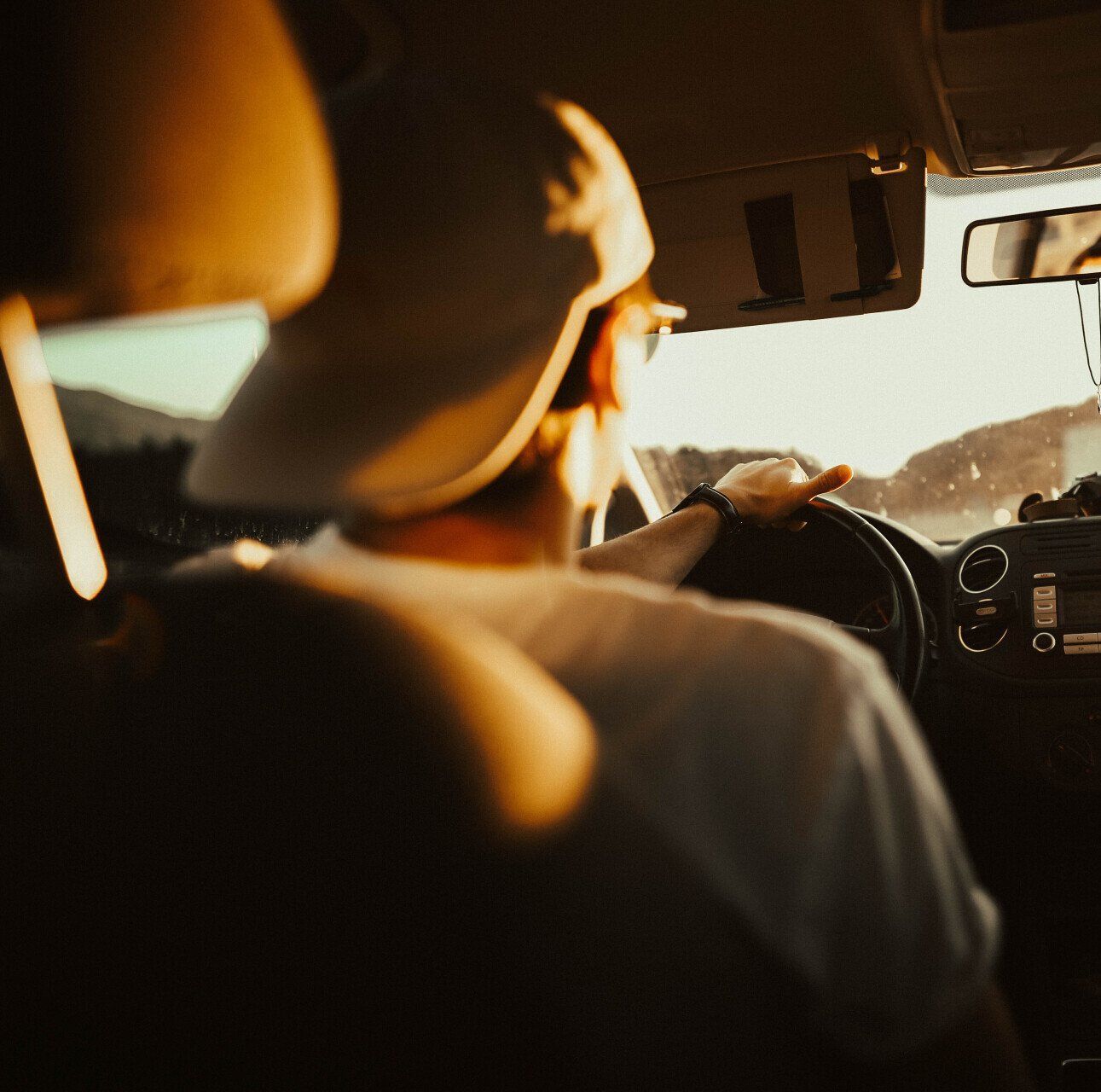 A man wearing a hat is driving a car