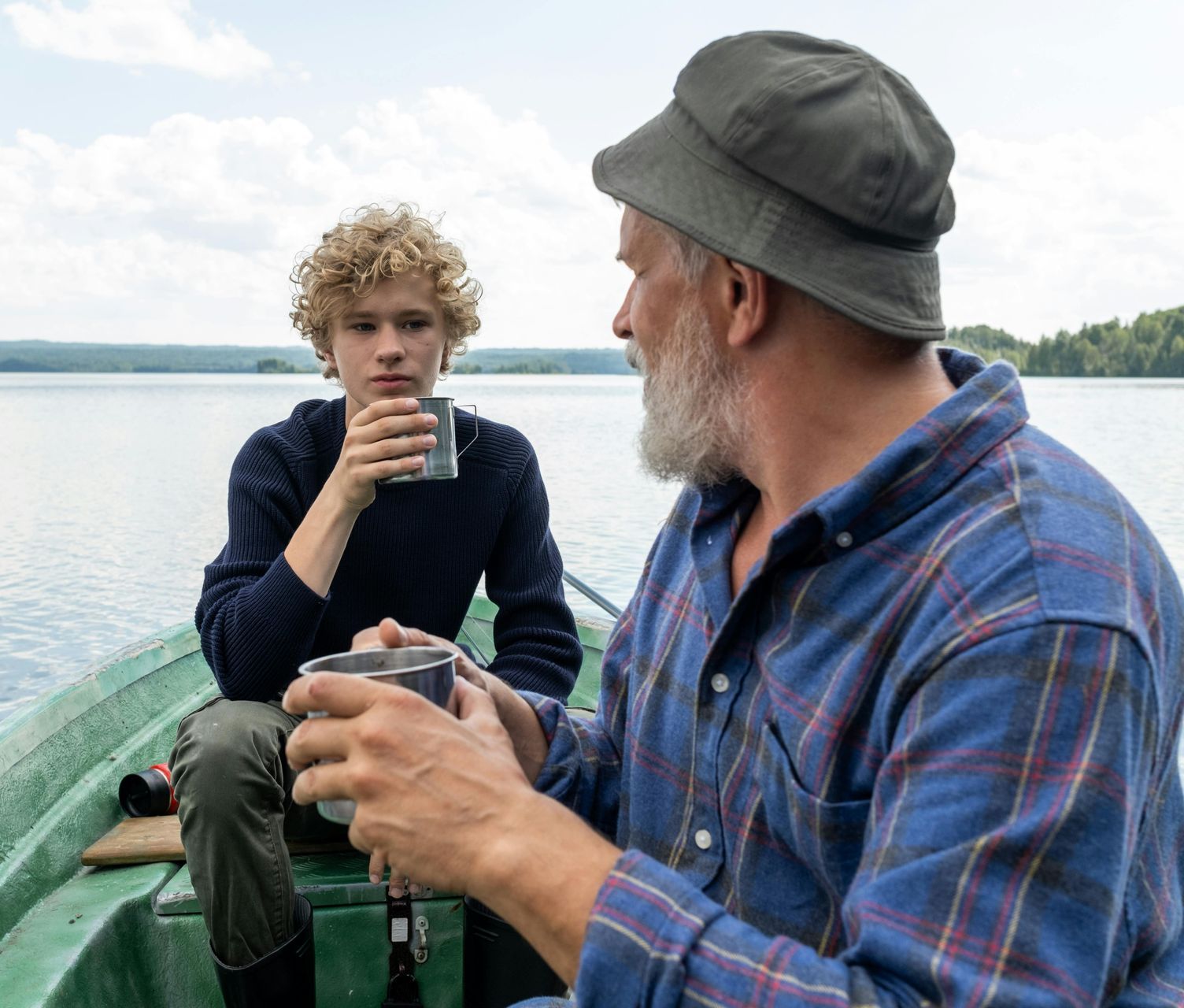 A man and a boy are sitting in a boat drinking coffee.