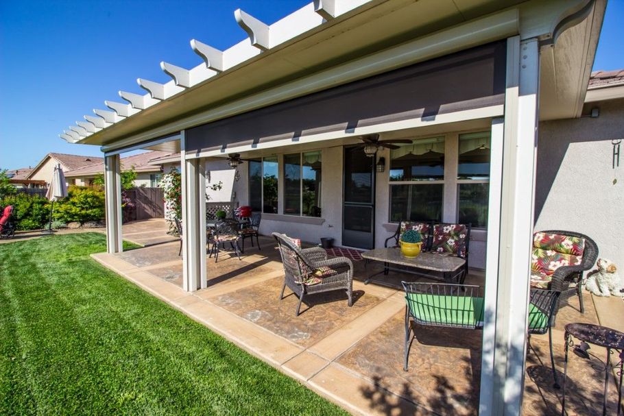 Covered patio with outdoor seating beside a lawn and house windows.