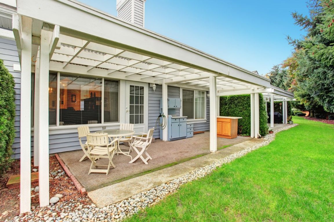 Covered patio with white outdoor table and chairs beside a house, overlooking a green lawn