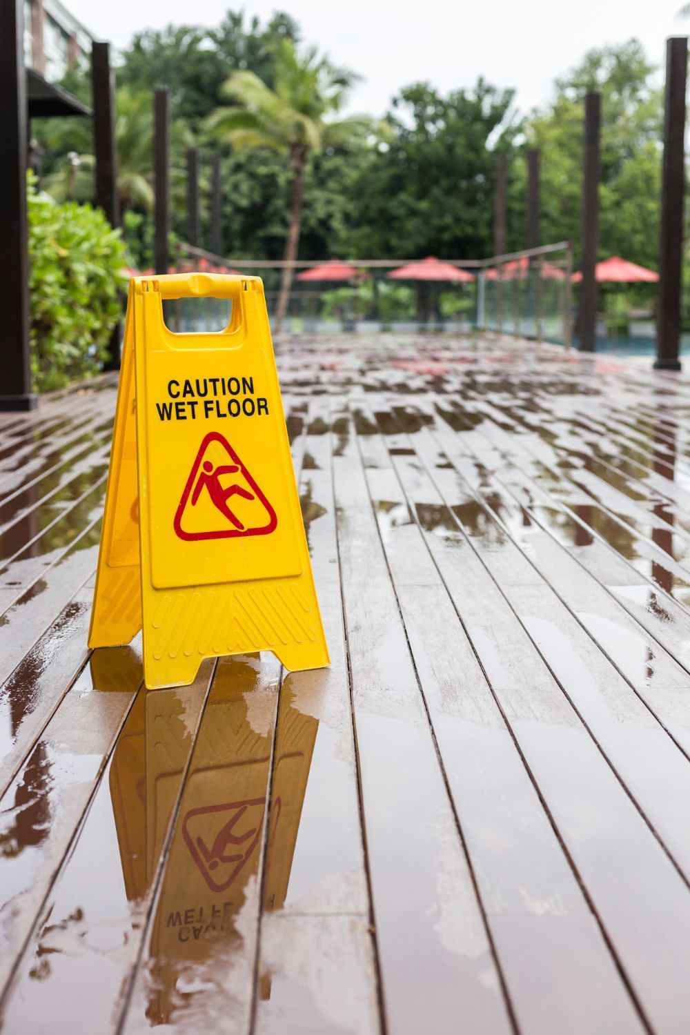 A yellow caution wet floor sign is on a wet wooden deck.