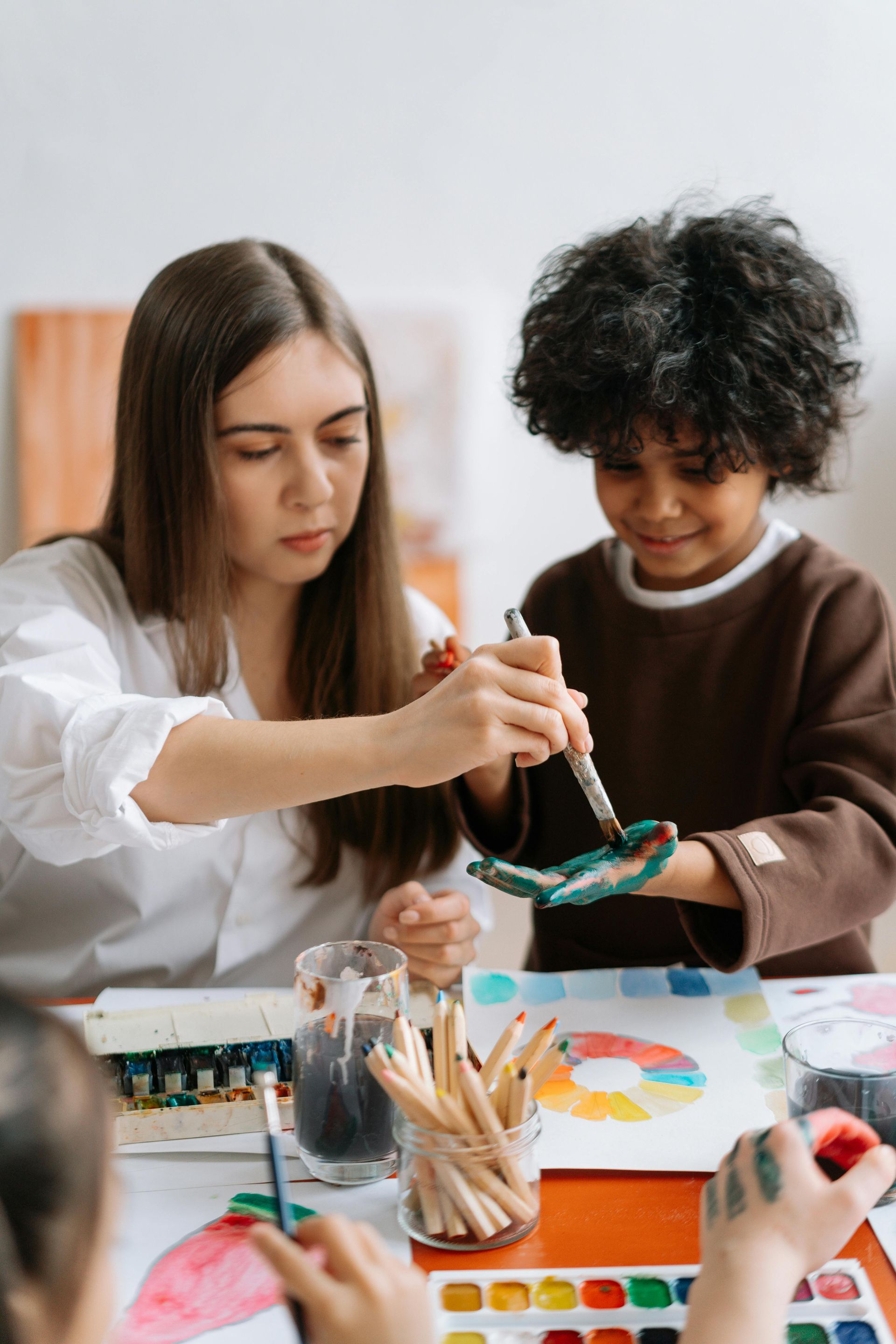 A woman is teaching a child how to paint with watercolors.