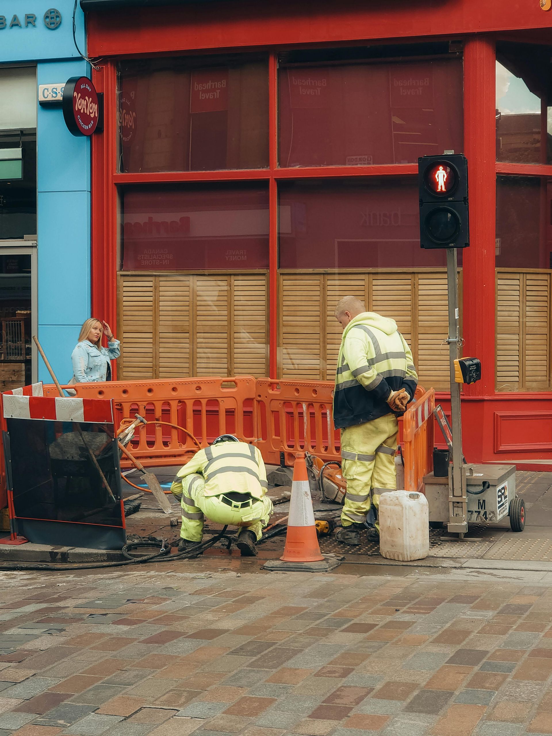 A group of construction workers are working on the sidewalk in front of a building.