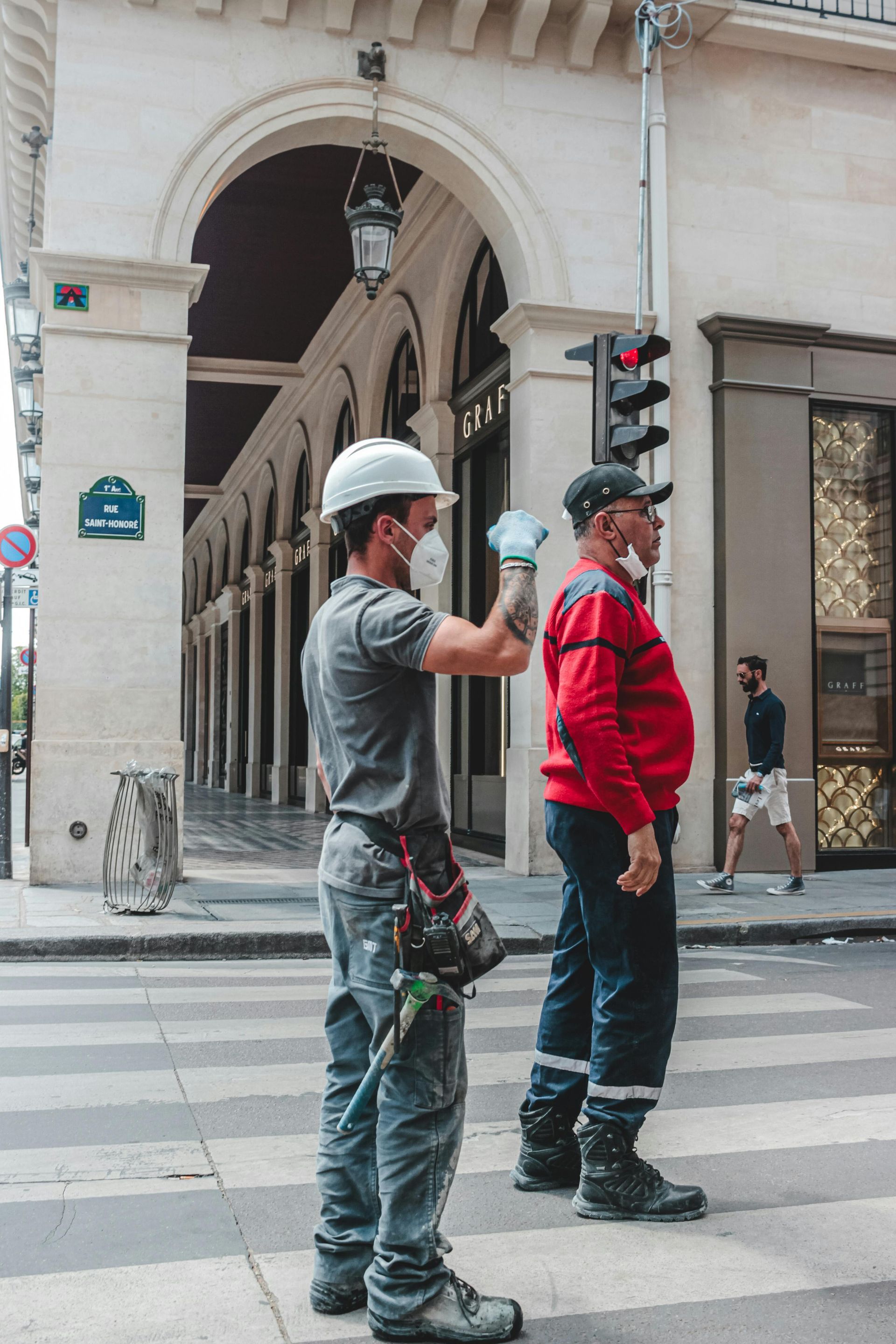 Two men wearing hard hats and gloves are standing on a street.