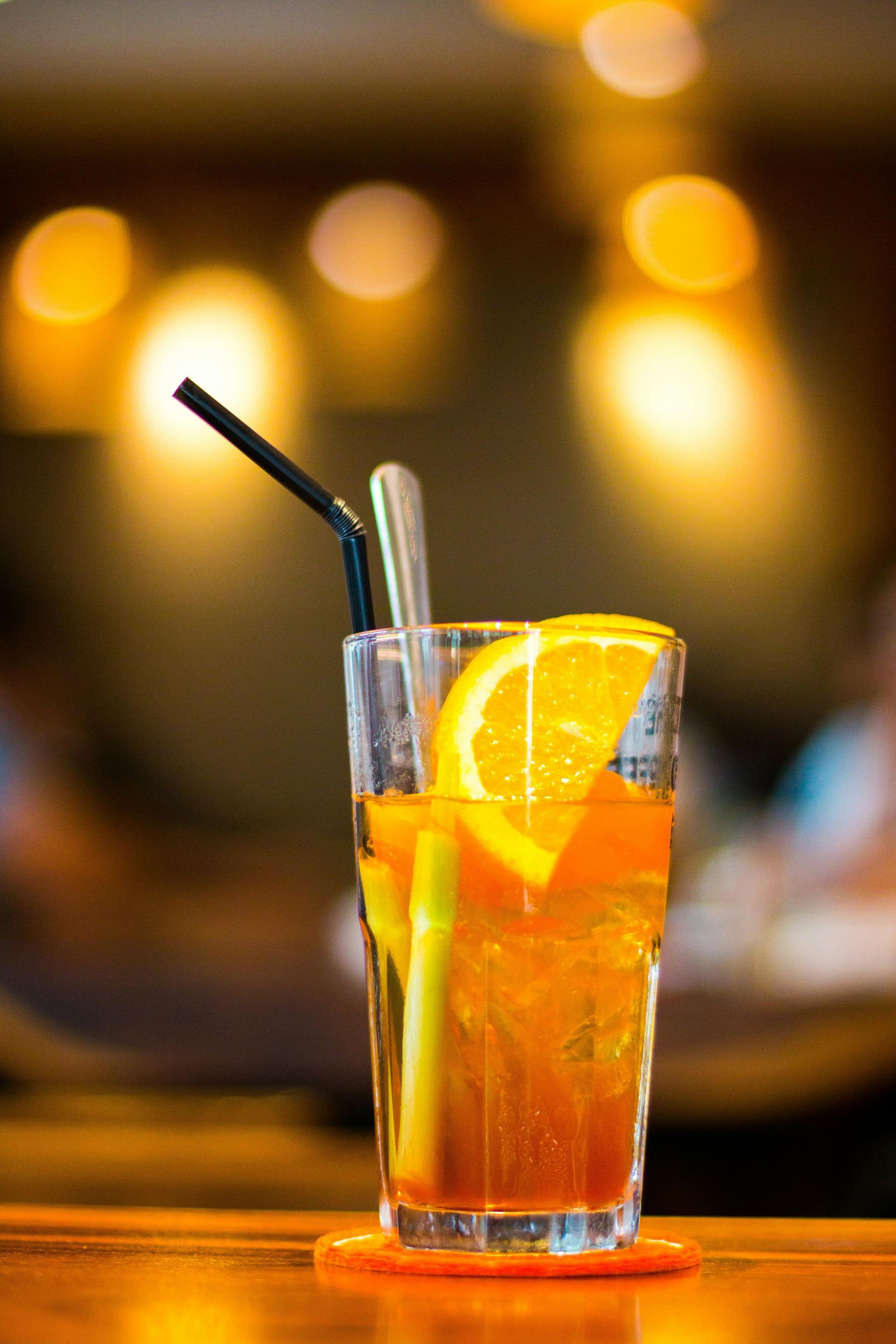 A close up of a glass of orange juice with a straw on a table.