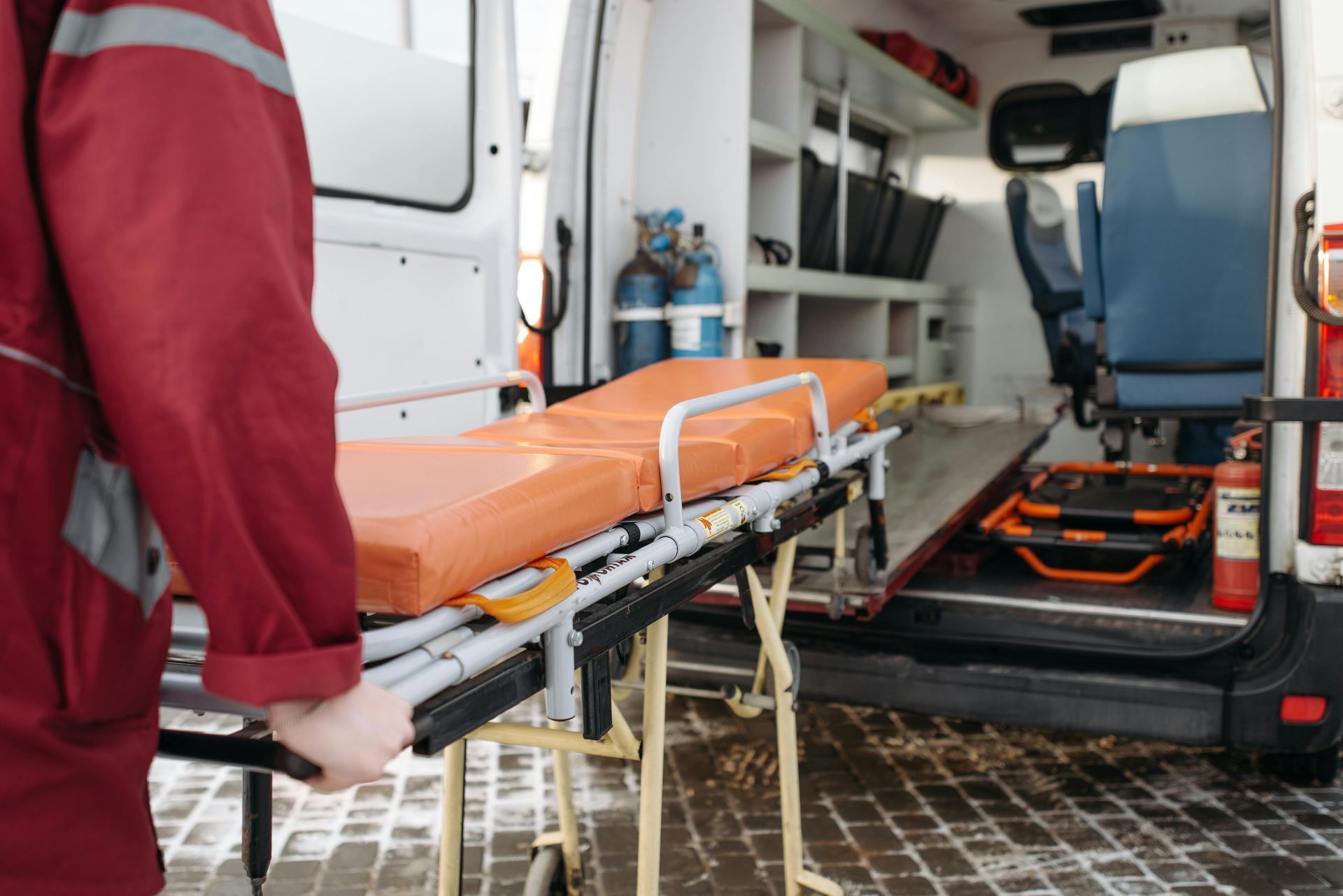 A man is holding an ambulance stretcher in front of an ambulance.