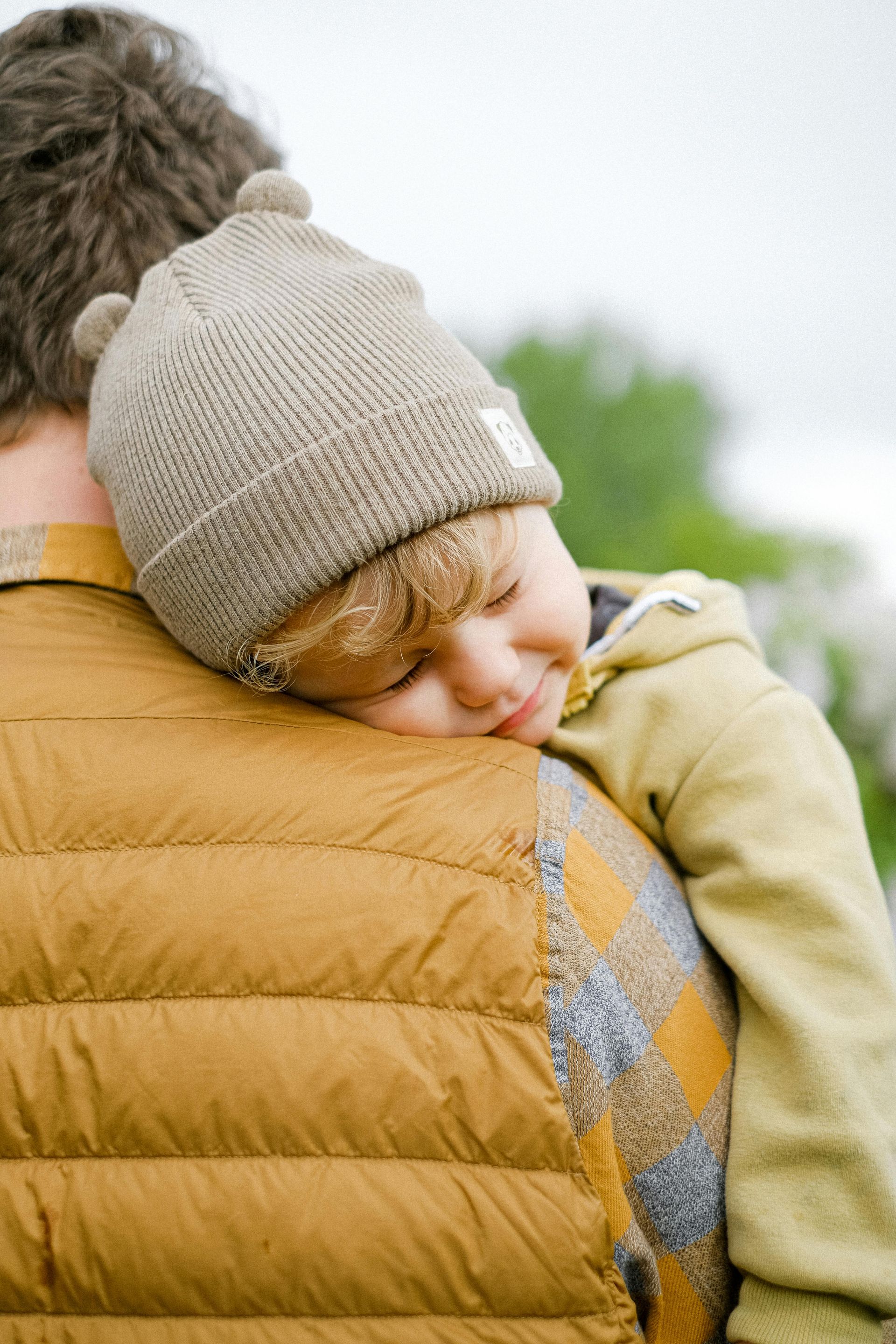 A little boy is sleeping on a man 's shoulder.