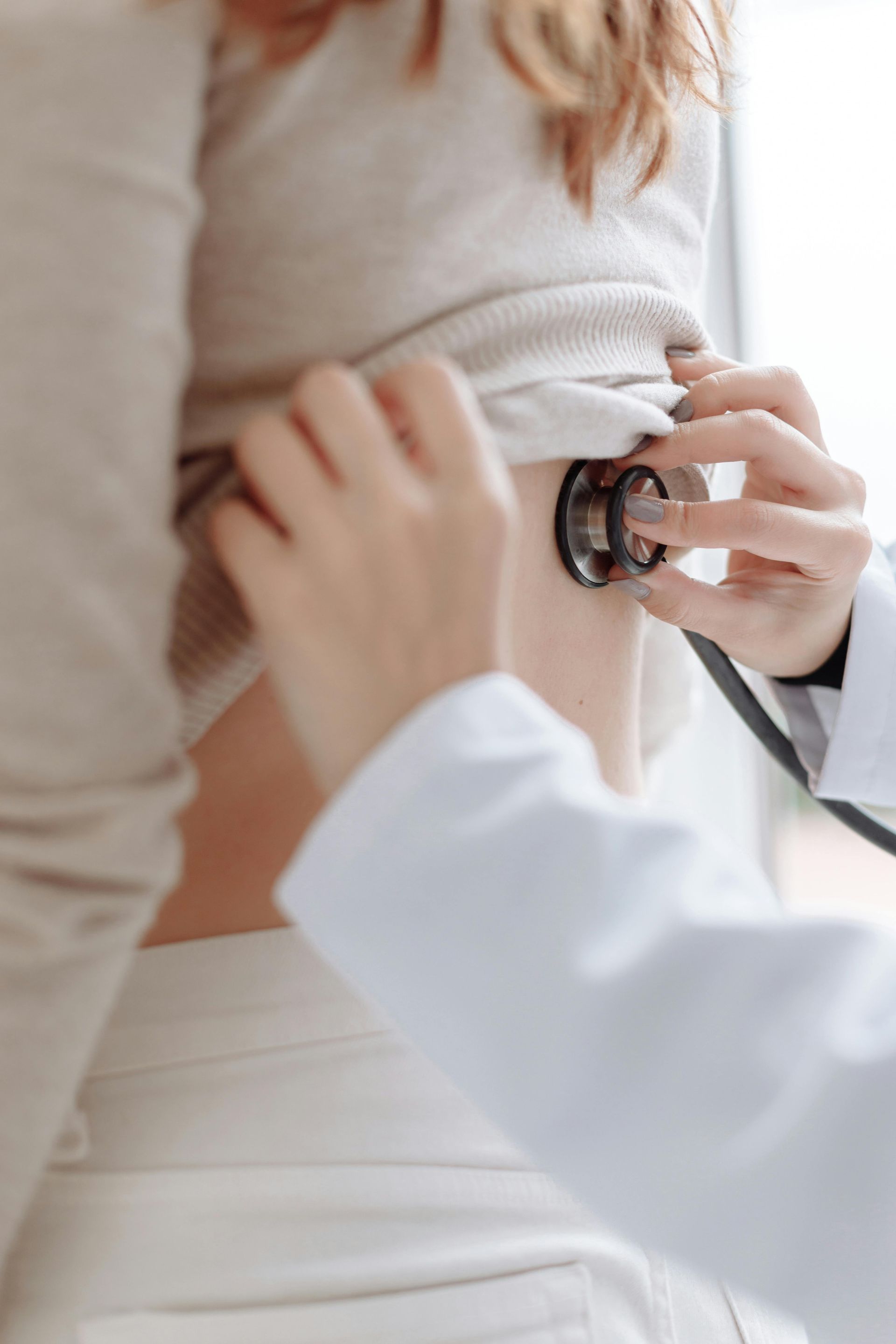 A doctor is listening to a woman 's chest with a stethoscope.