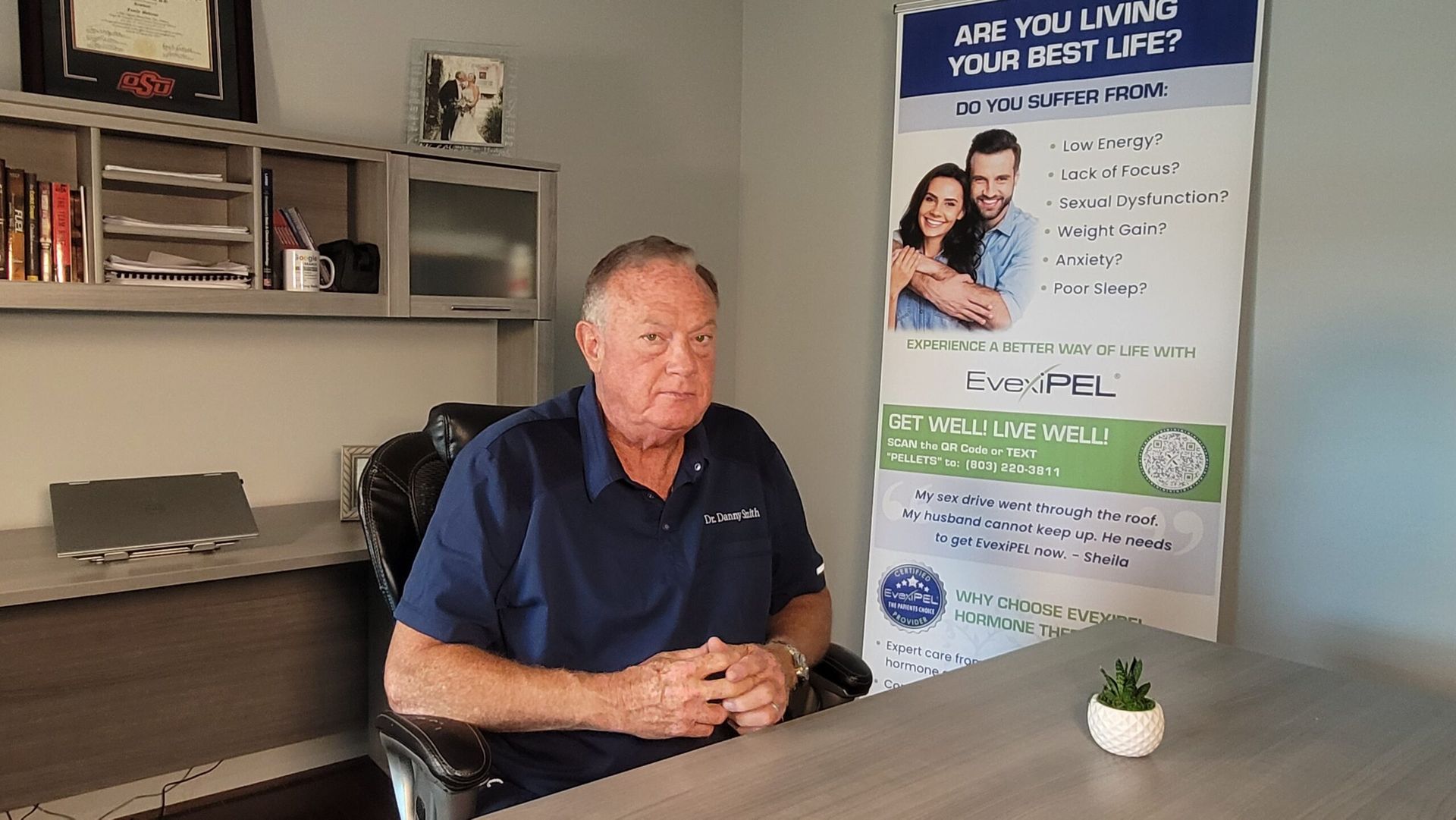 A man is sitting at a desk in front of a poster.