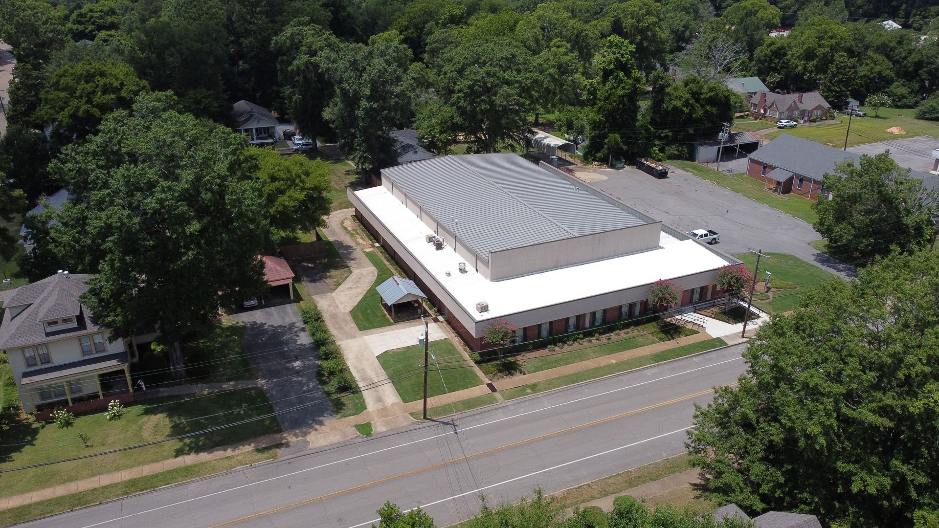 An aerial view of a large building with a white roof surrounded by trees.