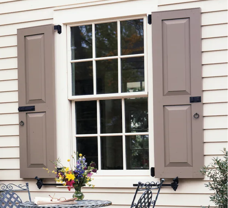 White house window with taupe shutters and a flower arrangement on the patio table