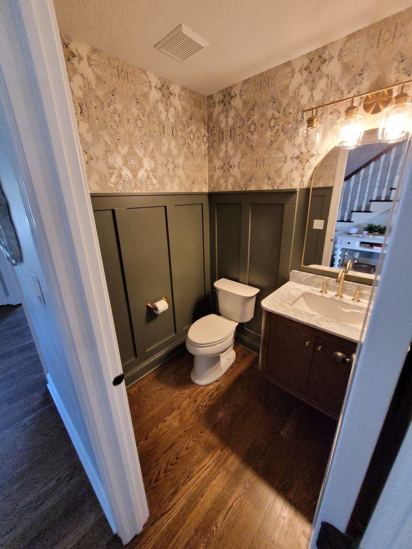 Bathroom with toilet, dark vanity, floral wallpaper, and wood-look floor viewed through the doorway
