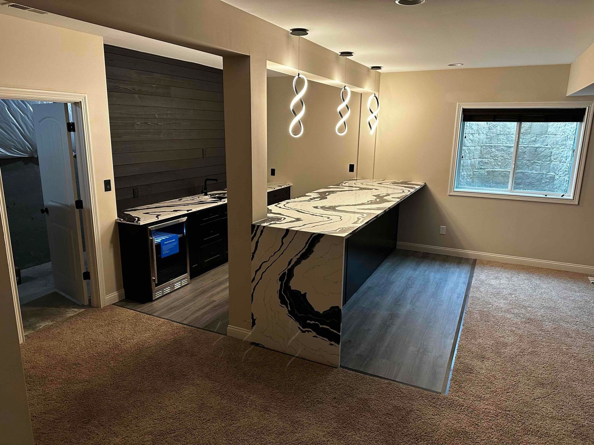 Open kitchen and living area with peninsula counter, pendant lights, and carpeted space by a window.