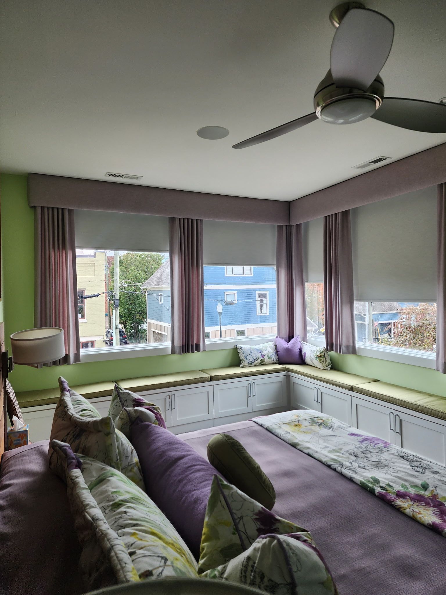 Bright bedroom with a bed, purple accents, bay windows, and a ceiling fan.