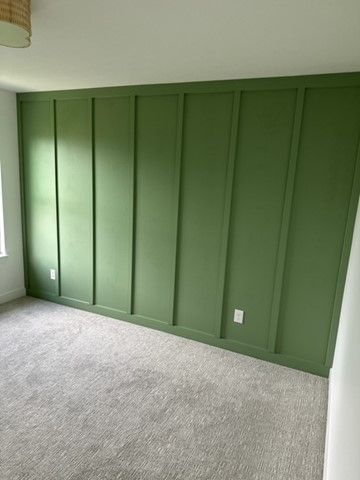 Empty room with green paneled accent wall and gray carpet near a window