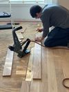 Person kneeling on a hardwood floor measuring wood planks with a power tool during installation