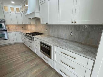 Modern white kitchen with gray countertops, stainless appliances, and wood-look flooring
