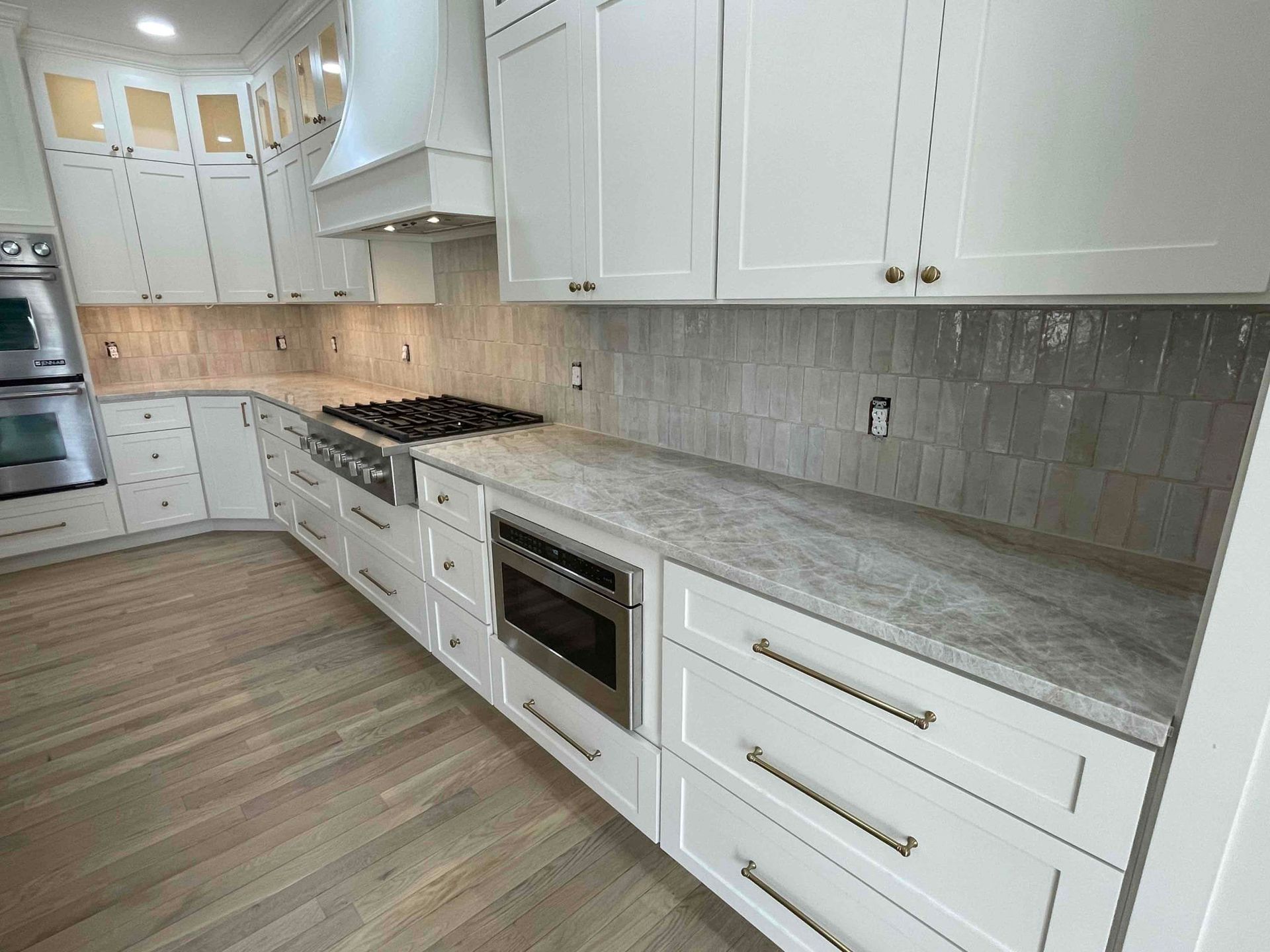 White kitchen with long countertops, stainless stove, and light wood flooring