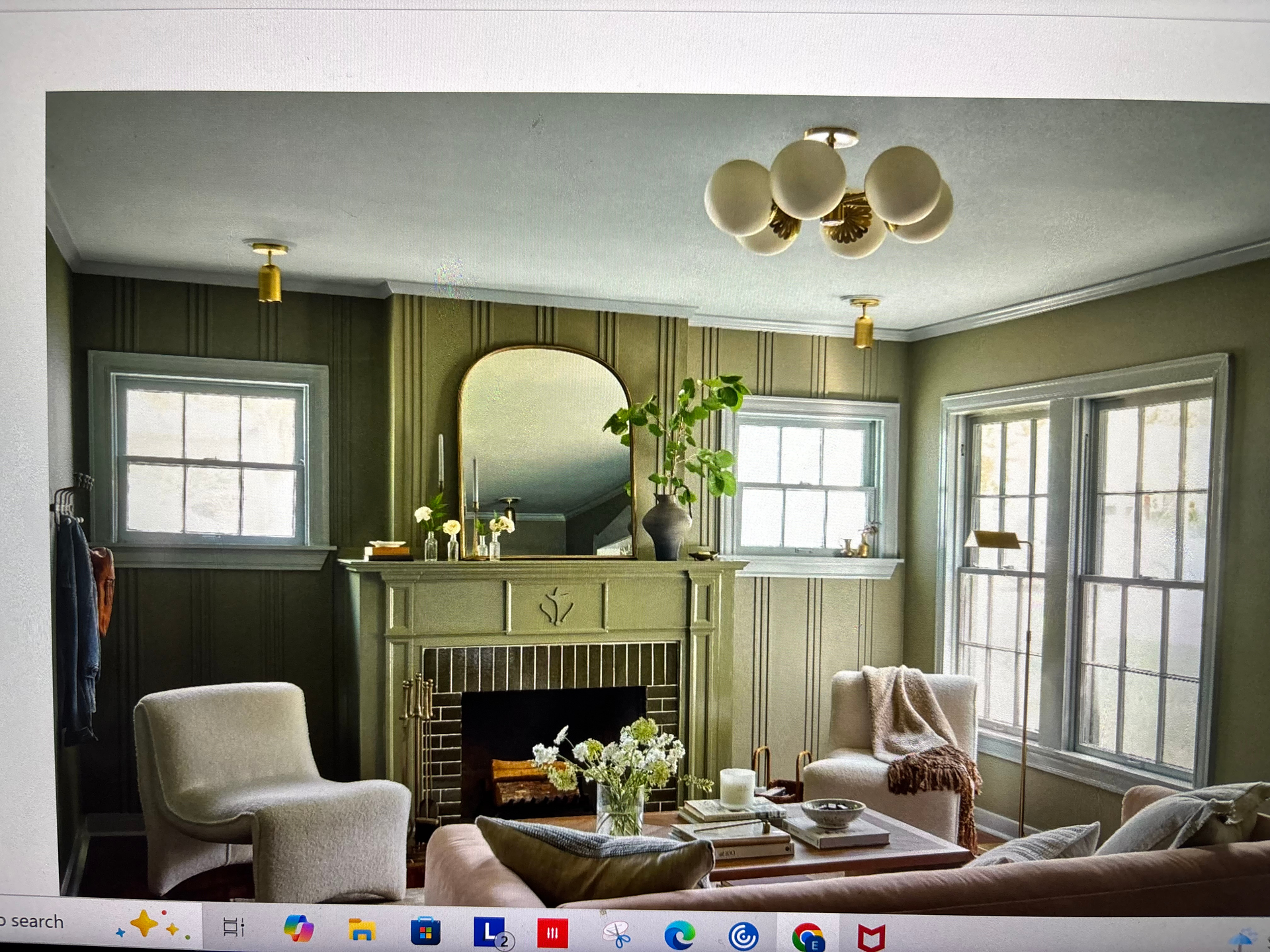 Cozy living room with fireplace, green walls, cream chairs, large windows, and a coffee table with flowers and books