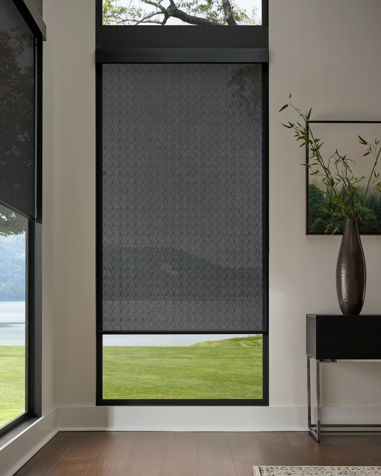 Modern interior with a dark roller shade covering a tall window and a small side table with vase and plant.