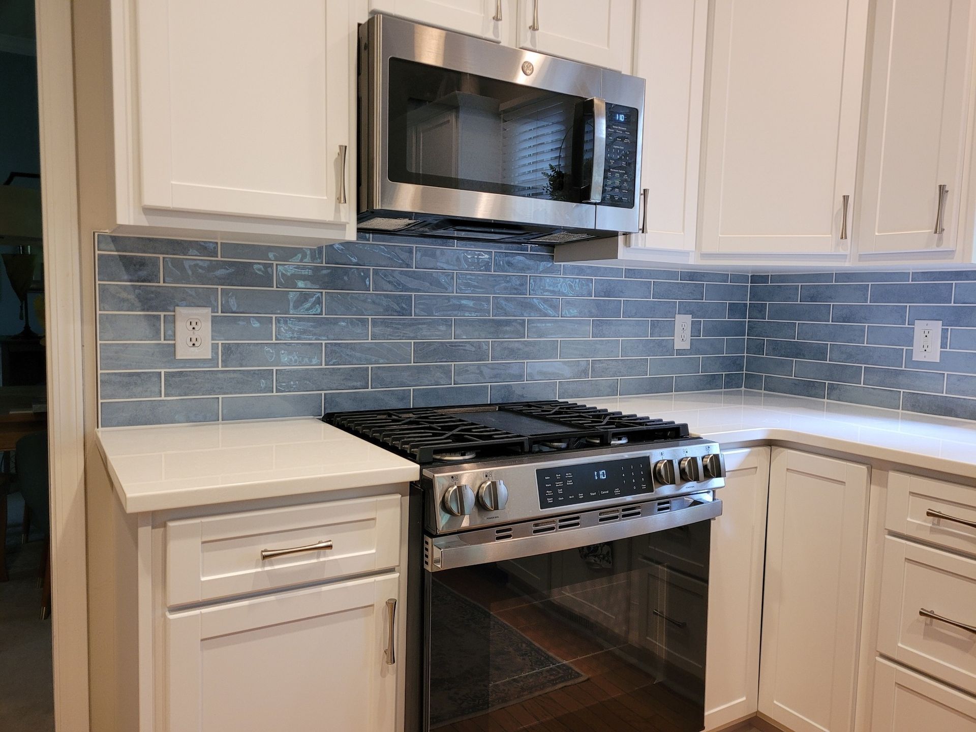 Modern kitchen with white cabinets, blue tile backsplash, stainless steel microwave, and gas stove.