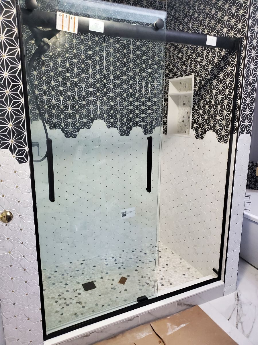 Black-framed glass shower enclosure with patterned curtain and towel bar above