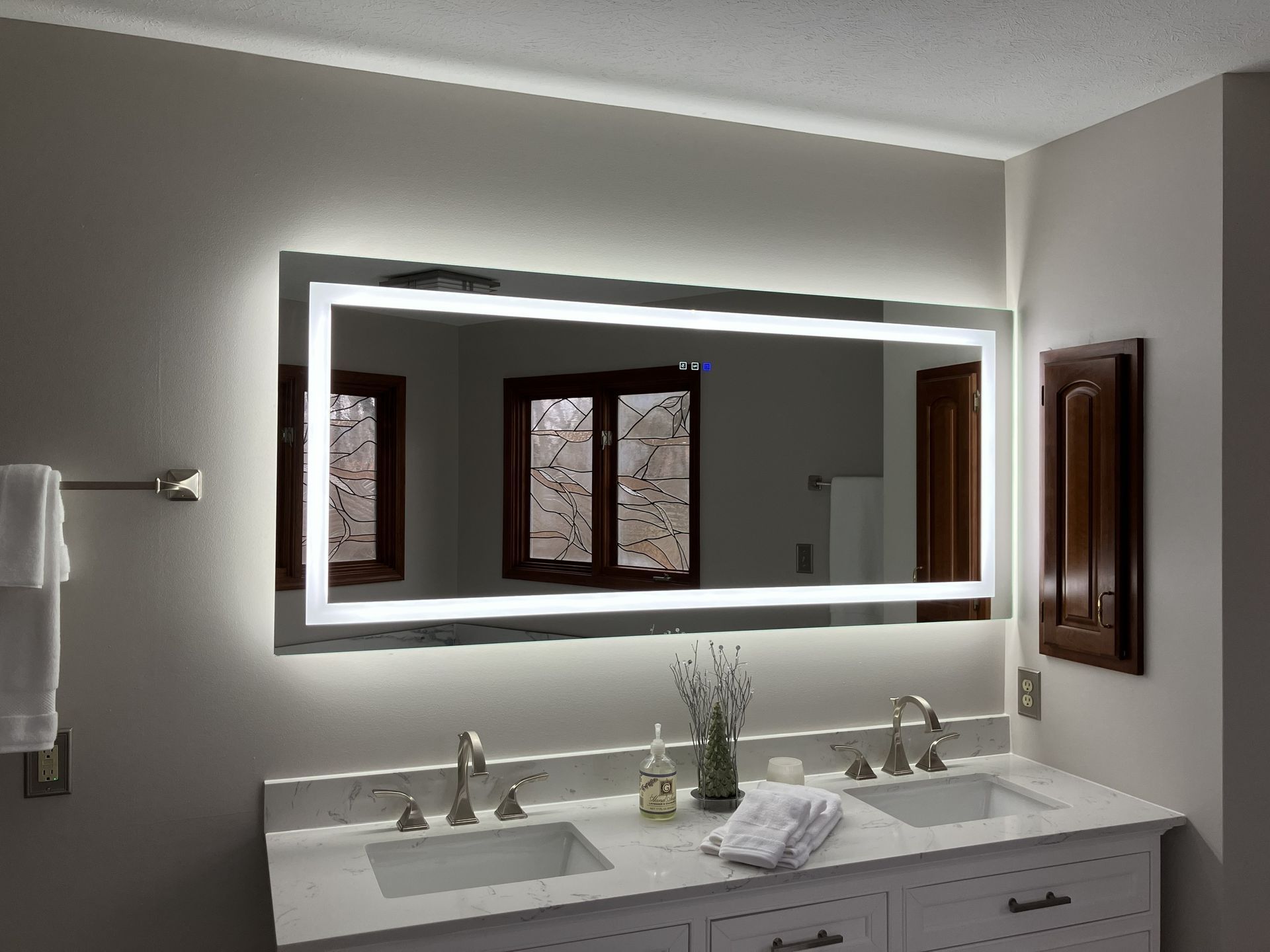 Modern bathroom with illuminated mirror, double sinks, and white marble countertop