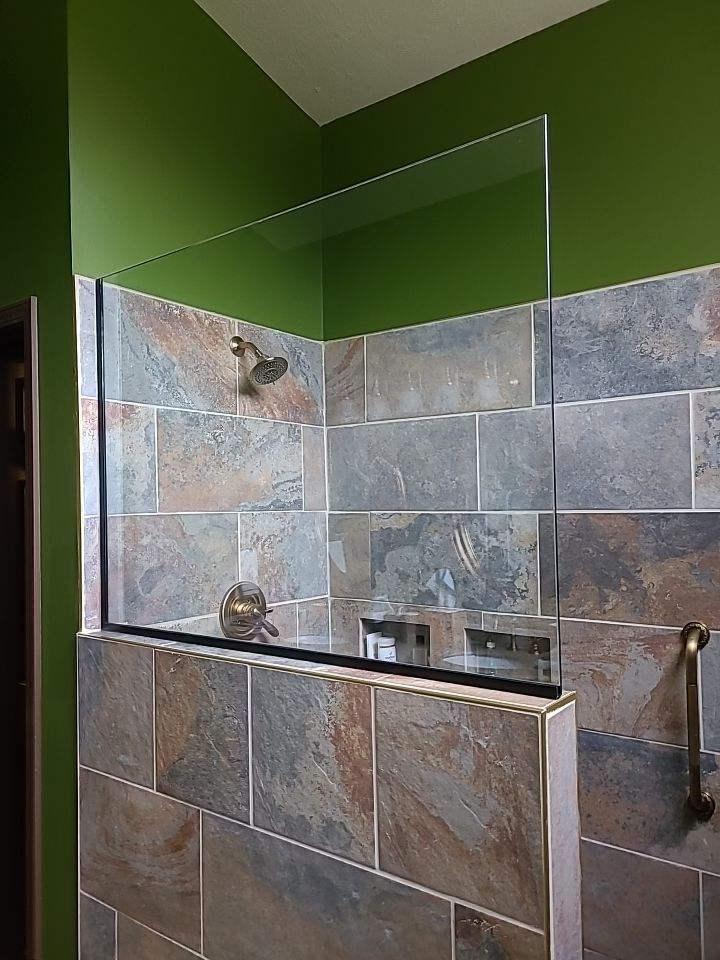 Stone-tiled shower with green walls, glass panel, and shower fixtures in a bathroom