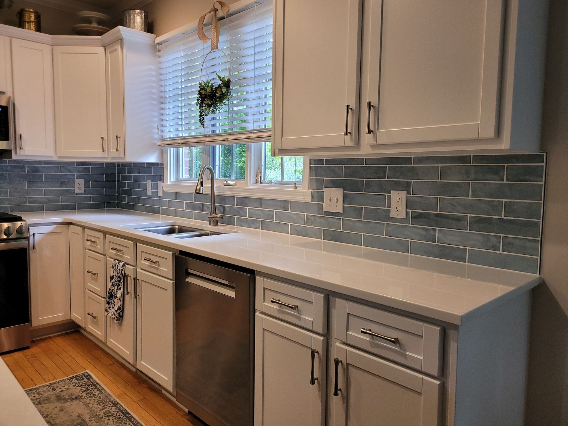 Bright white kitchen with gray tile backsplash, stainless dishwasher, and window over the sink.
