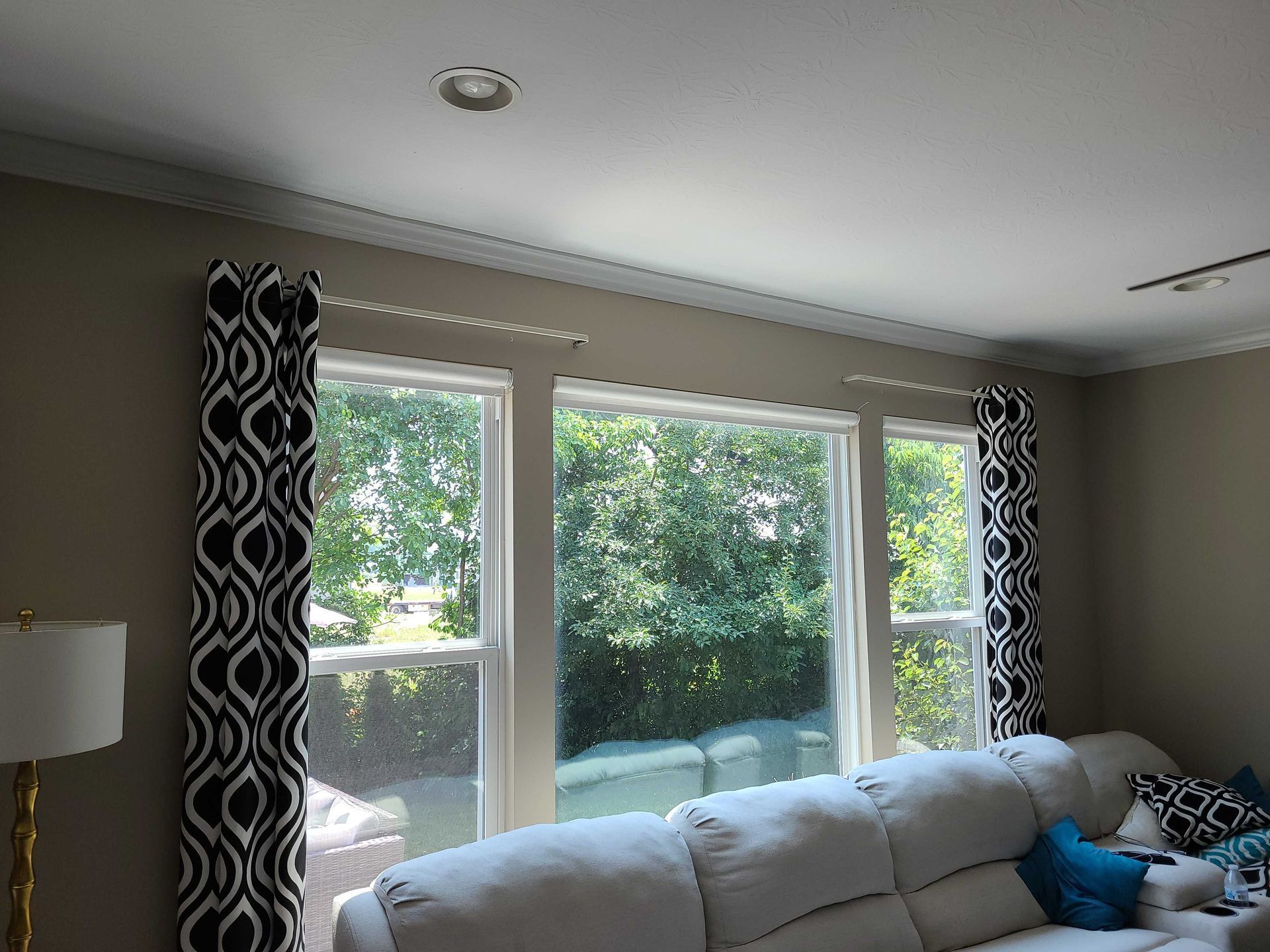 Living room with large windows, gray sofa, and patterned black-and-white curtains overlooking green trees