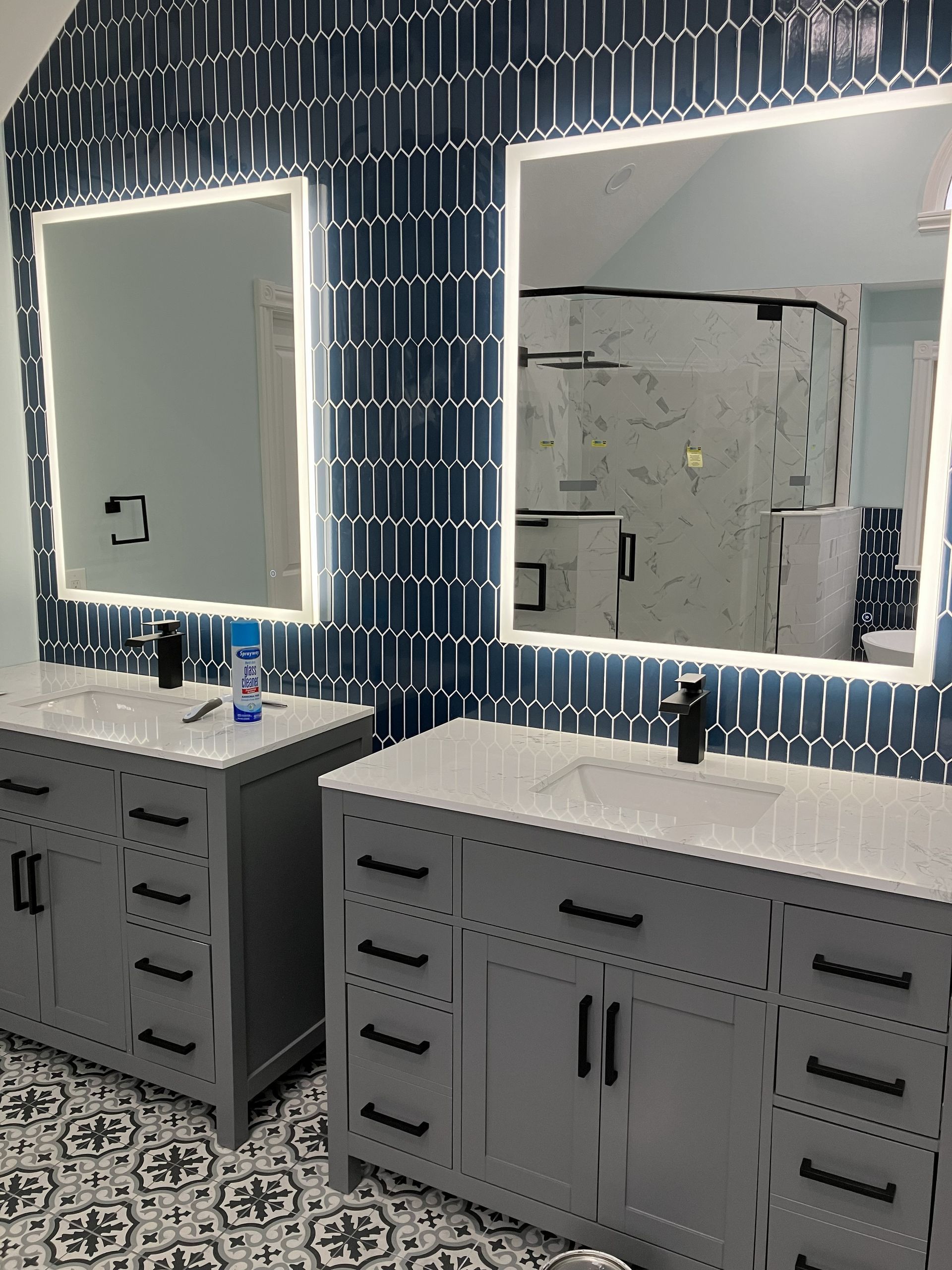 Modern bathroom vanity with two illuminated mirrors, gray cabinets, and blue patterned tile wall