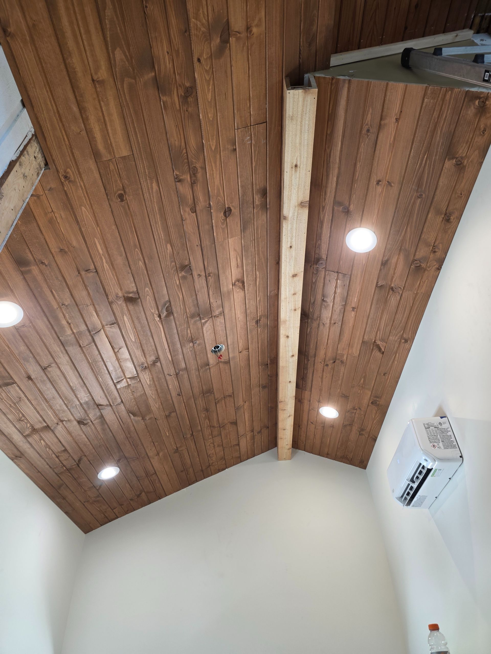 Wood-paneled vaulted ceiling with recessed lights and white walls in a room