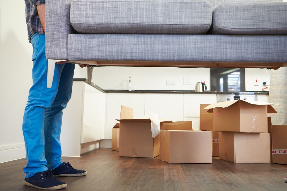 A man is carrying a couch in a living room filled with cardboard boxes — South Burnett Truck Rental In Chinchilla, QLD