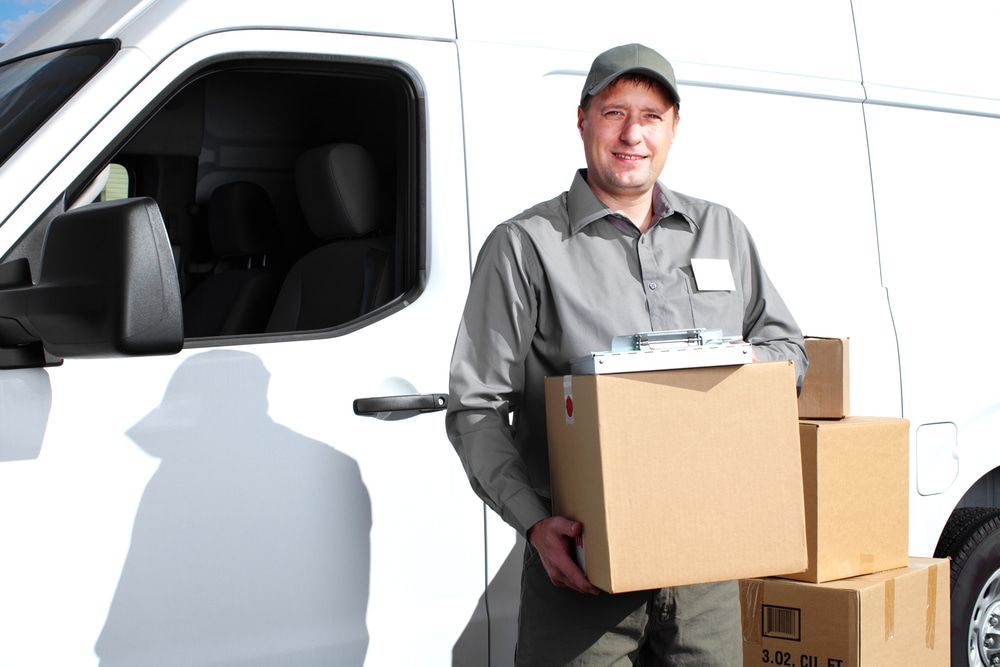 A Delivery Man Is Holding A Box In Front Of A White Van — South Burnett Truck Rental In Bundaberg, QLD
