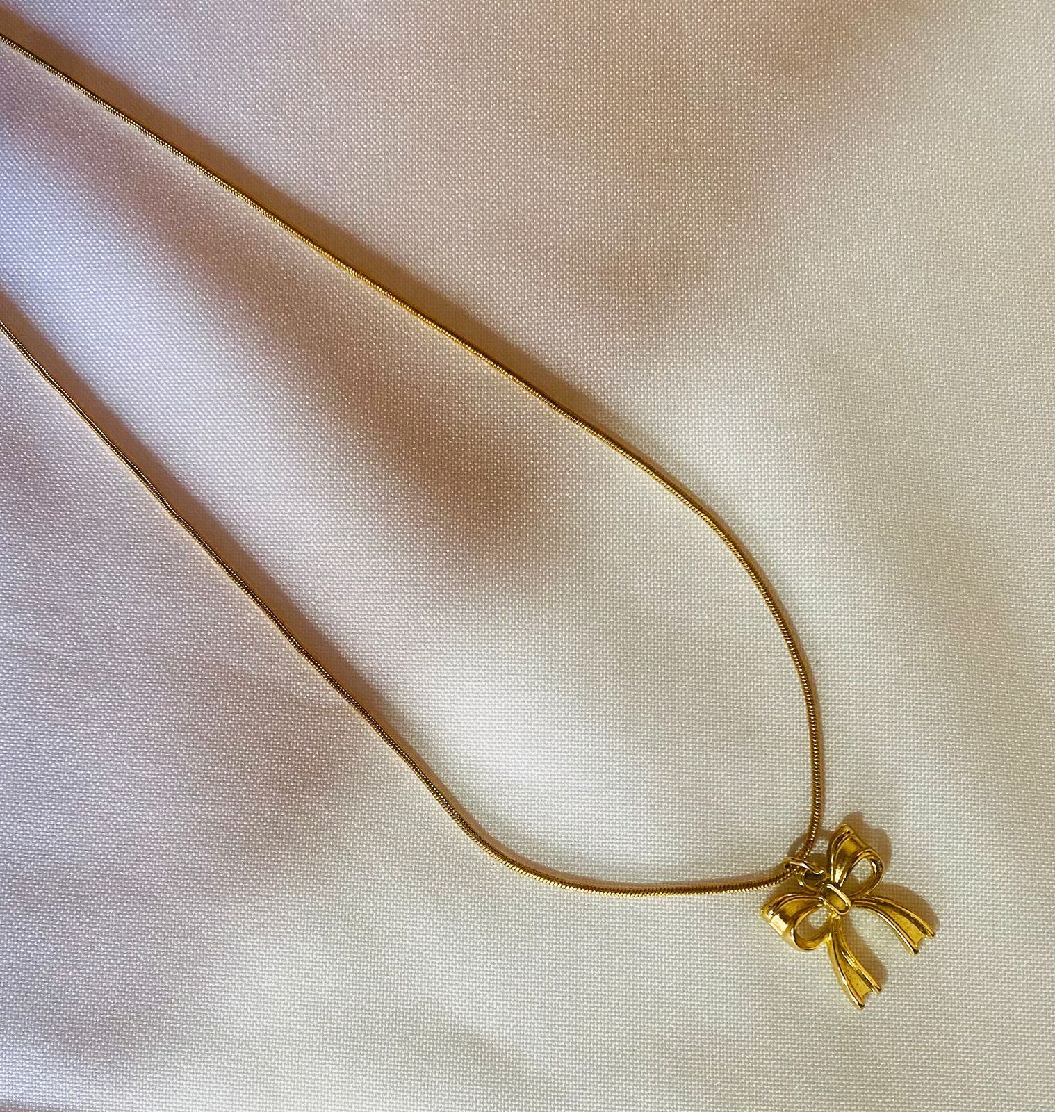 Un collar de oro con un colgante de lazo está sobre una tela blanca.