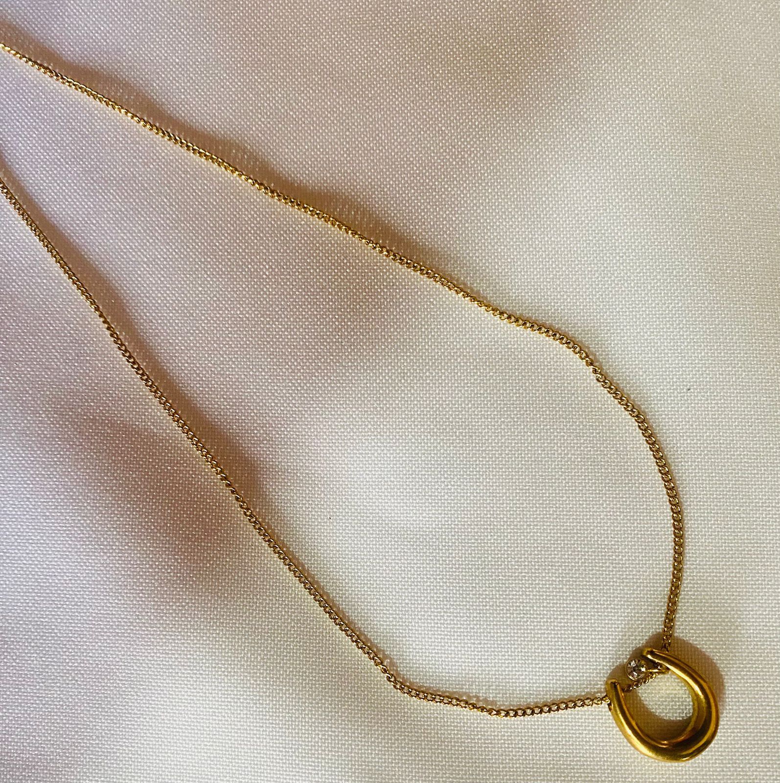 Un collar de oro con un colgante de herradura está sobre una tela blanca.