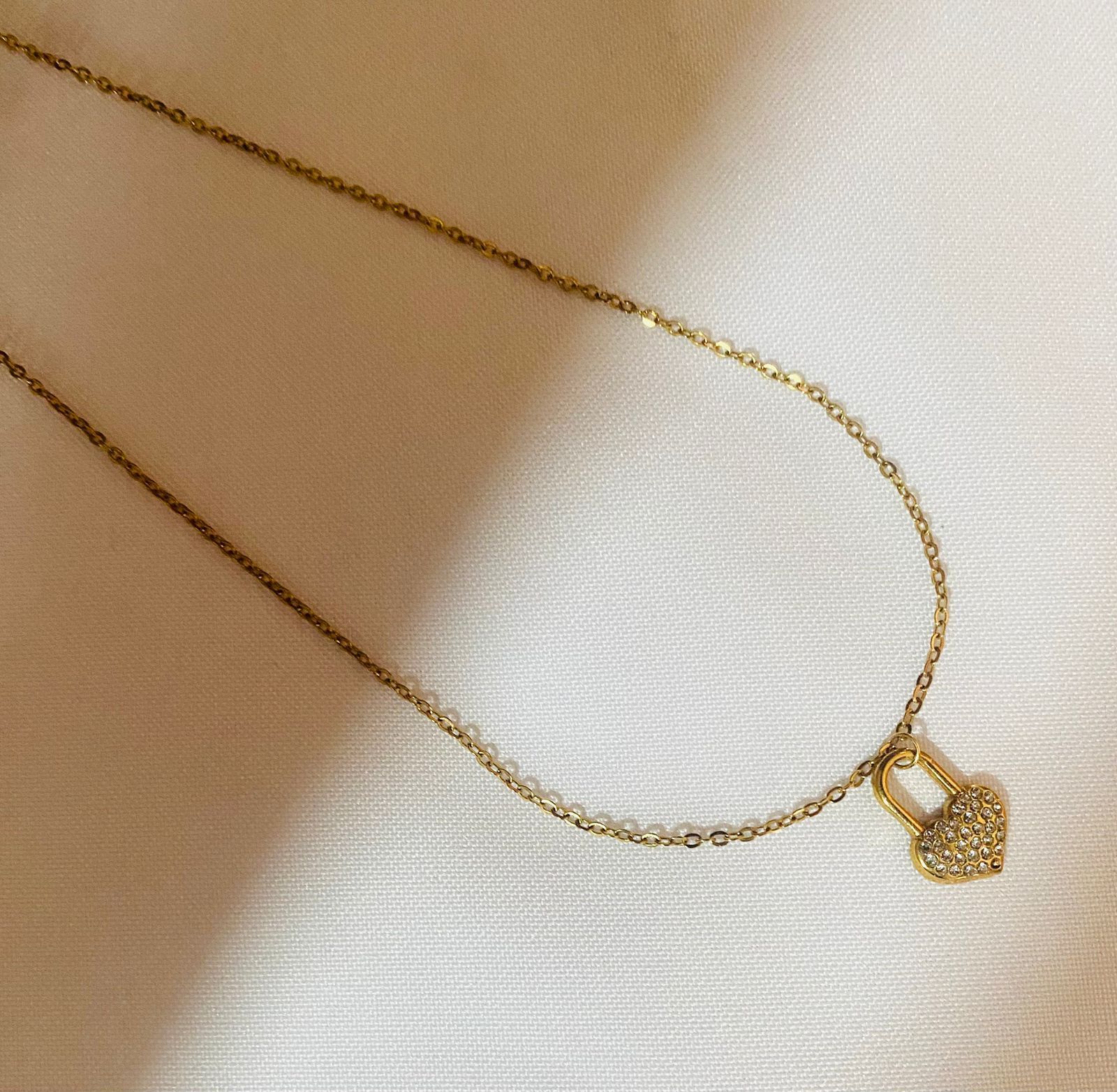 Un collar de oro con un colgante de candado en forma de corazón.