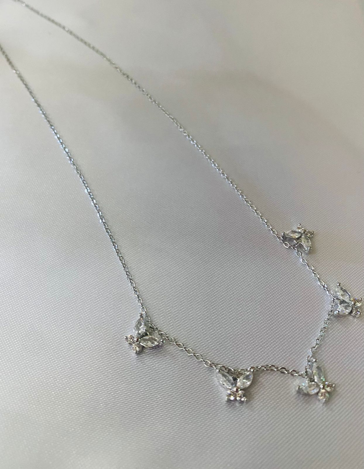 Un primer plano de un collar de plata con dijes de mariposas sobre una superficie blanca.