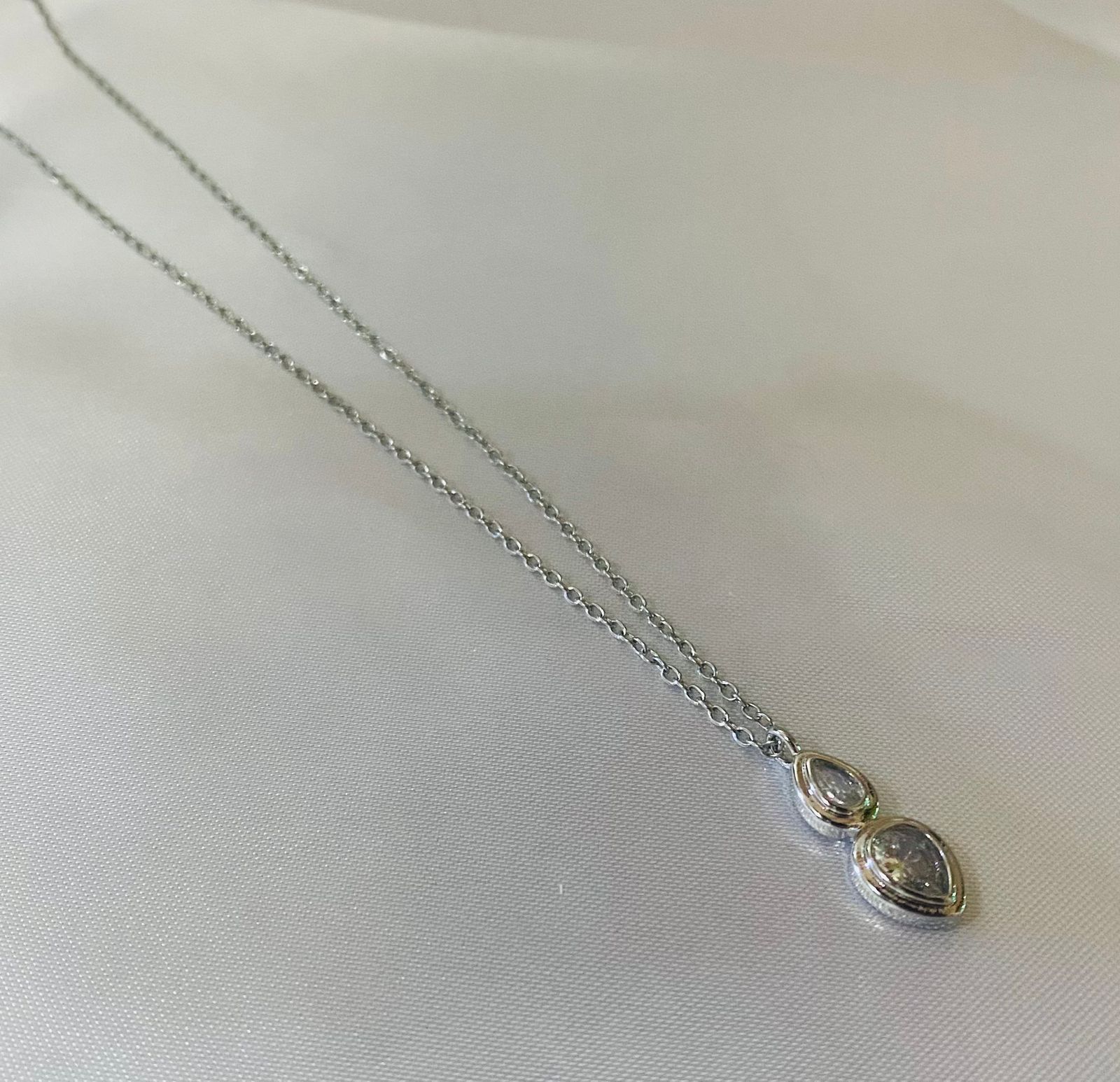 Un collar de plata con un colgante reposa sobre una tela blanca.