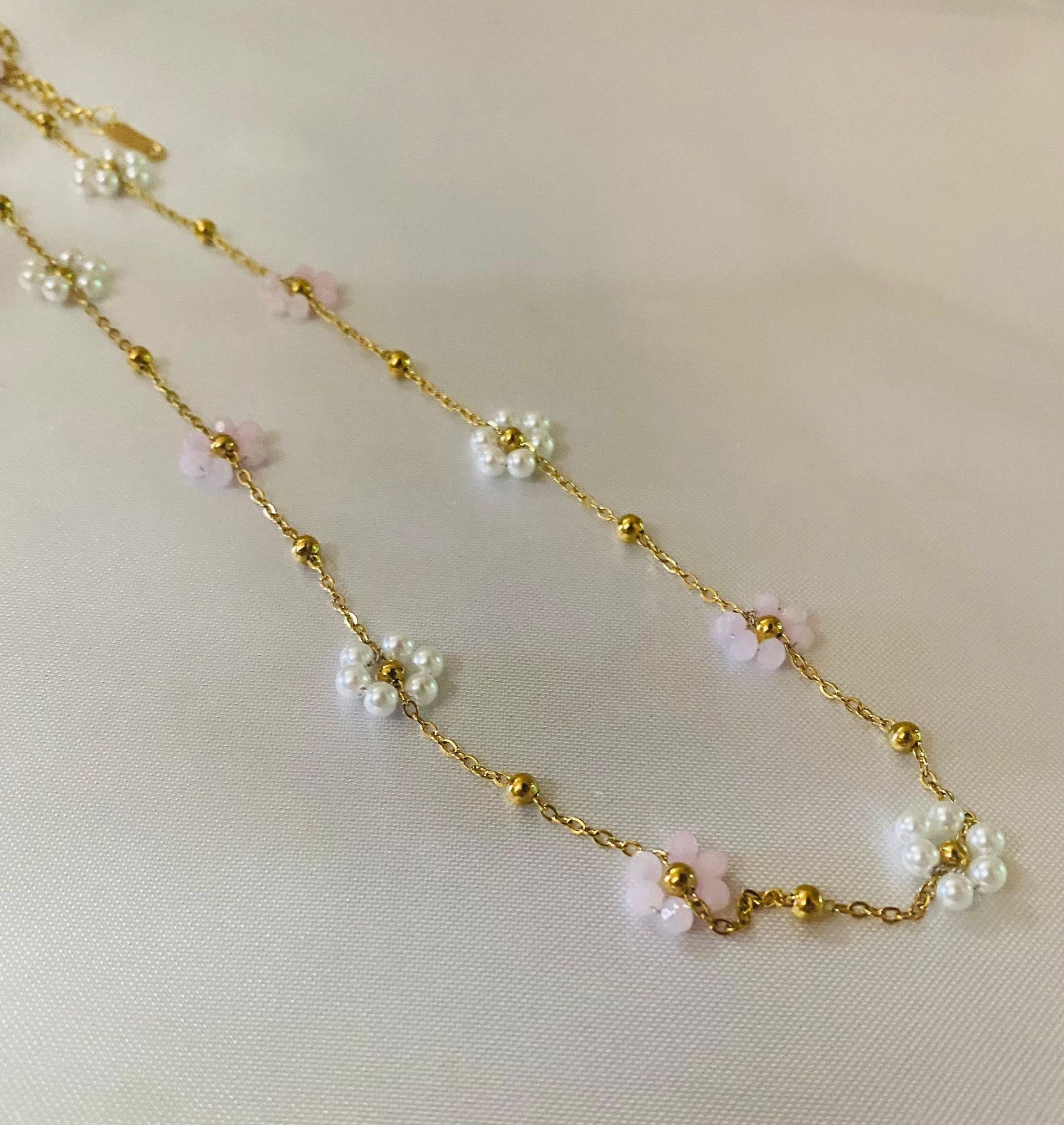 Un primer plano de un collar con flores y perlas sobre una superficie blanca.