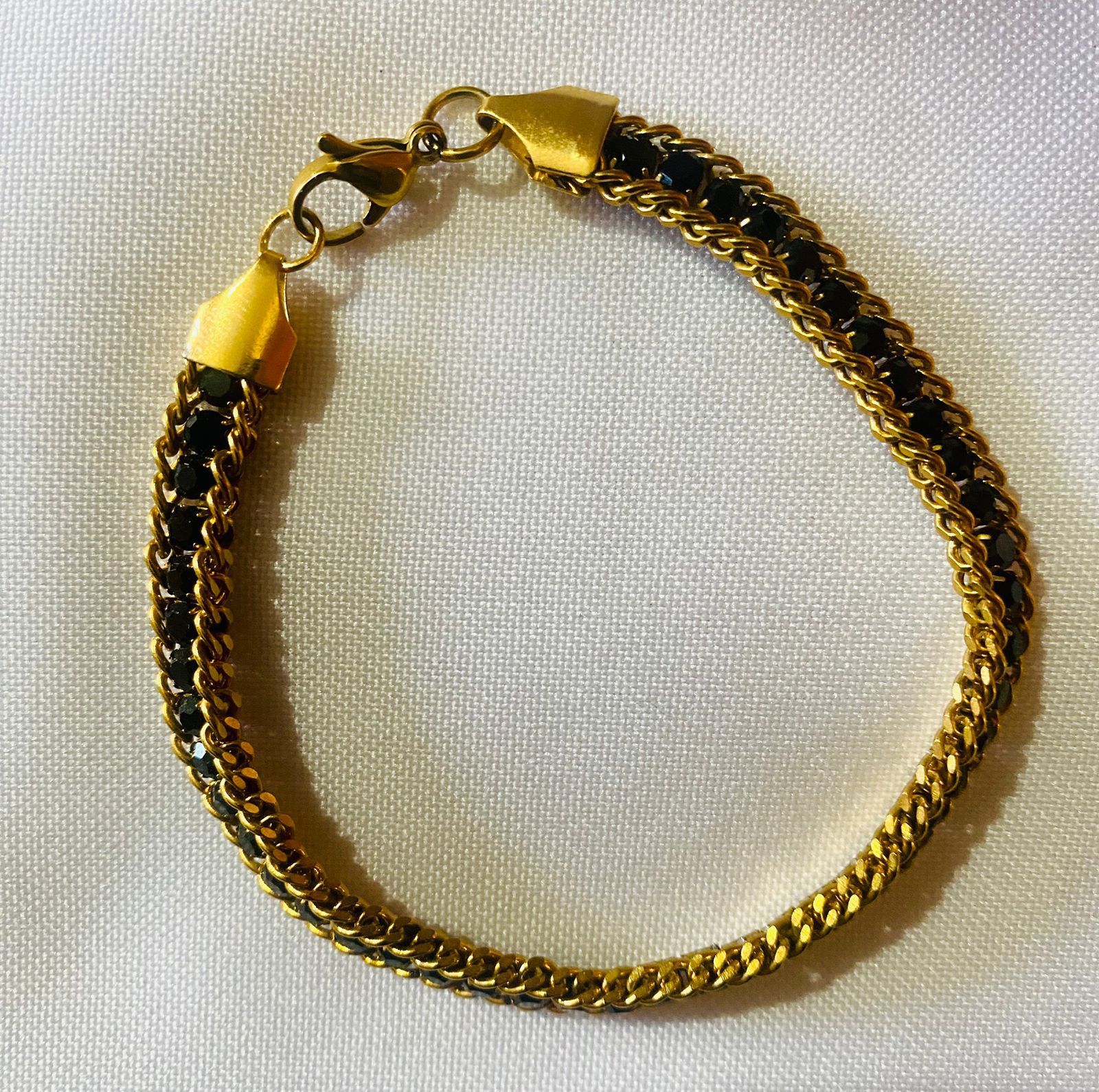 Una pulsera de oro con cuentas negras está sobre una tela blanca.