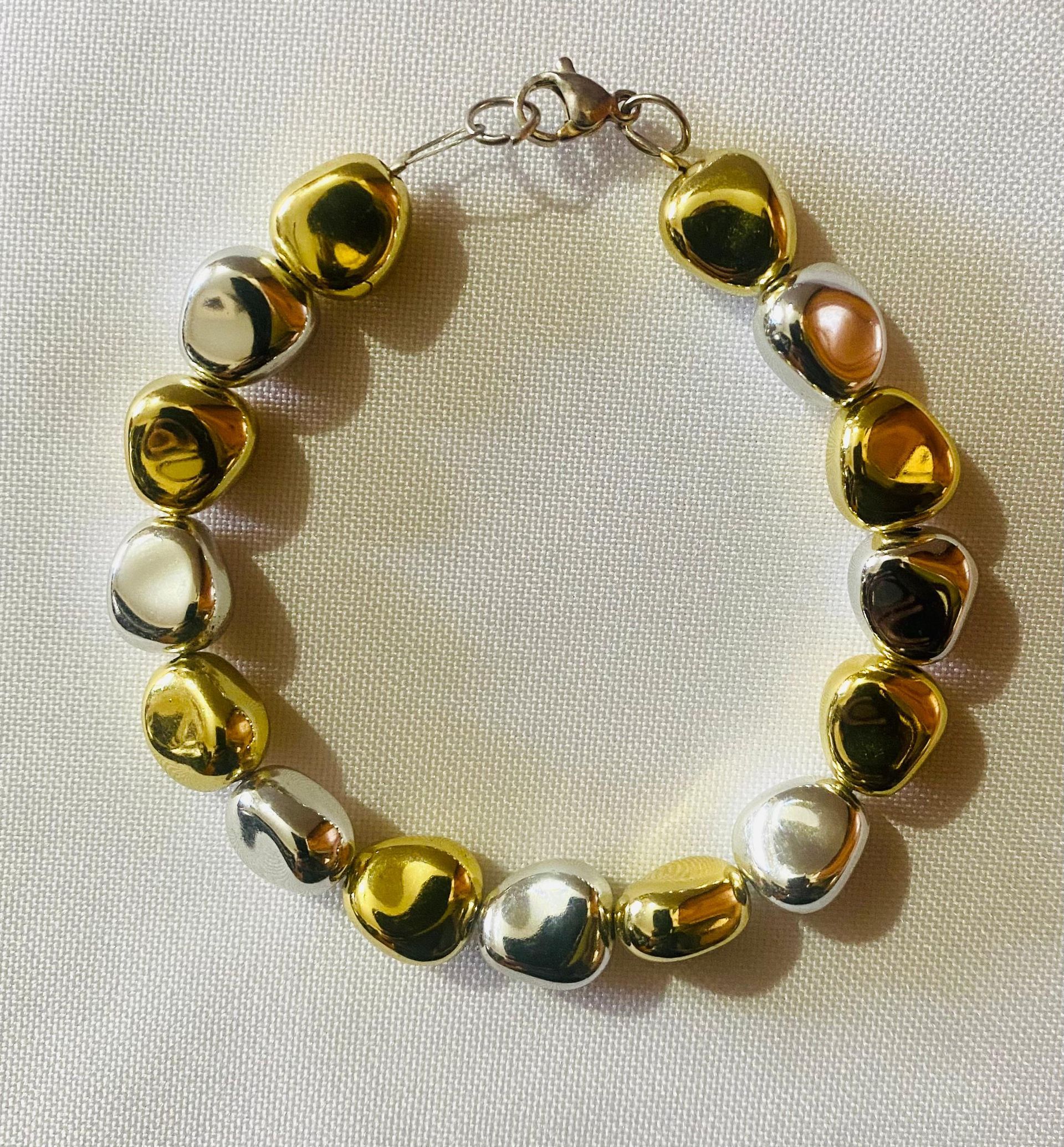 Una pulsera con cuentas de oro y plata sobre una tela blanca.