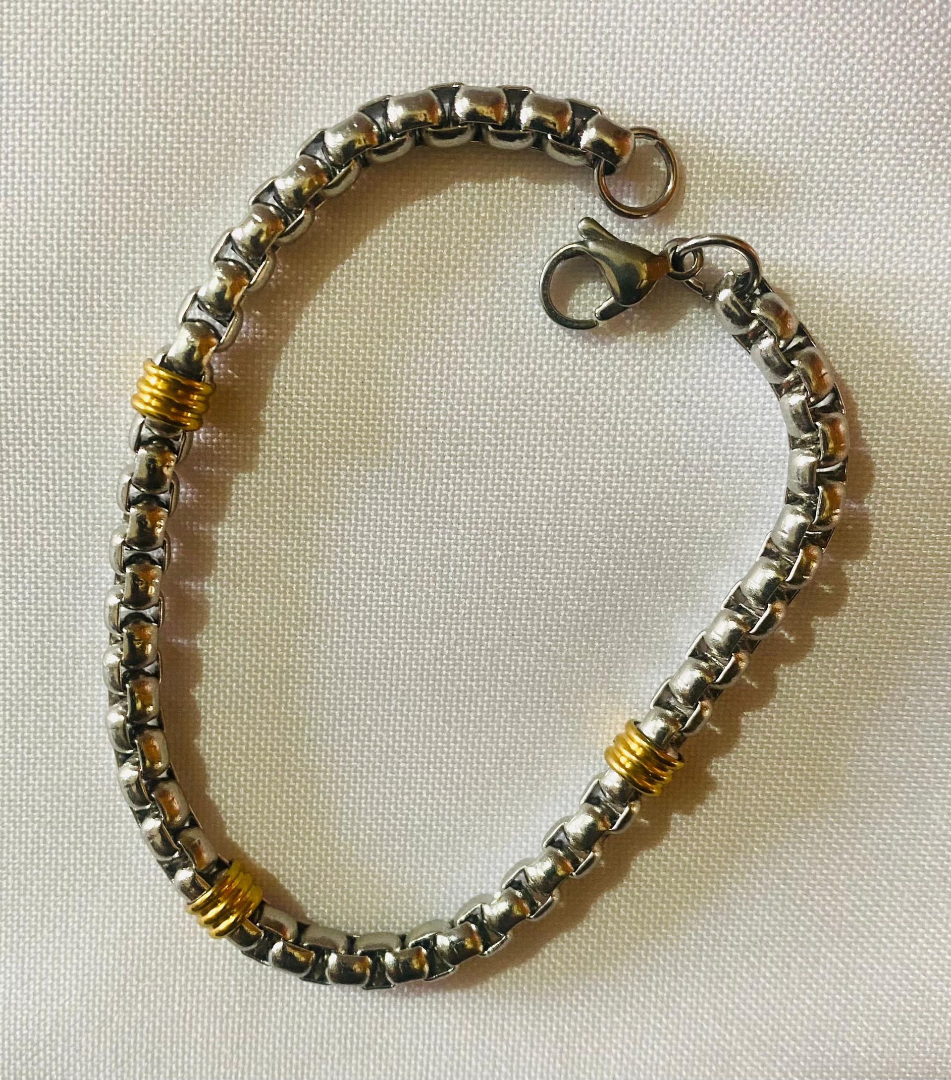 Una pulsera de plata y oro reposa sobre un paño blanco.