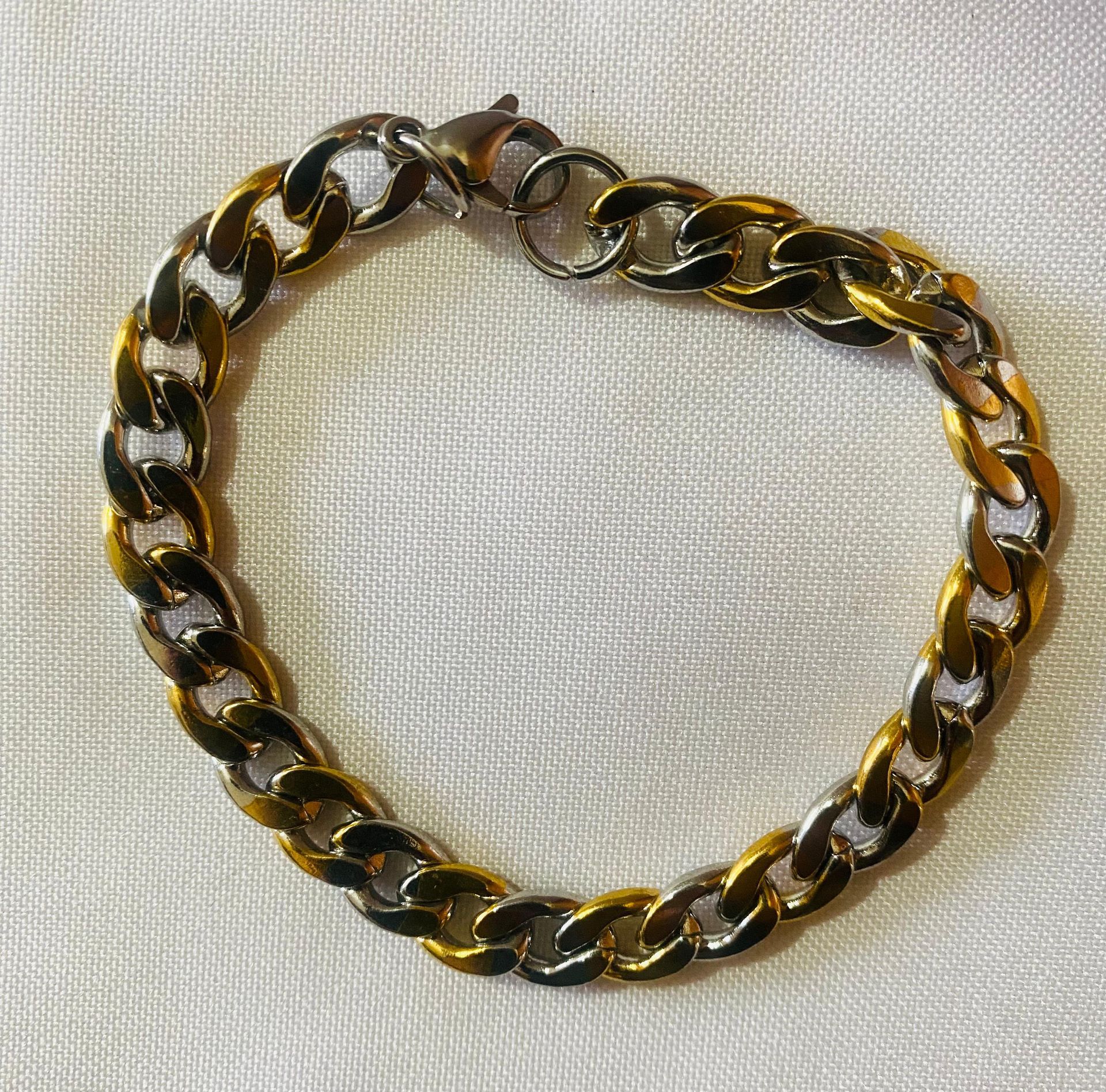Una pulsera de cadena de oro y plata está sobre una tela blanca.