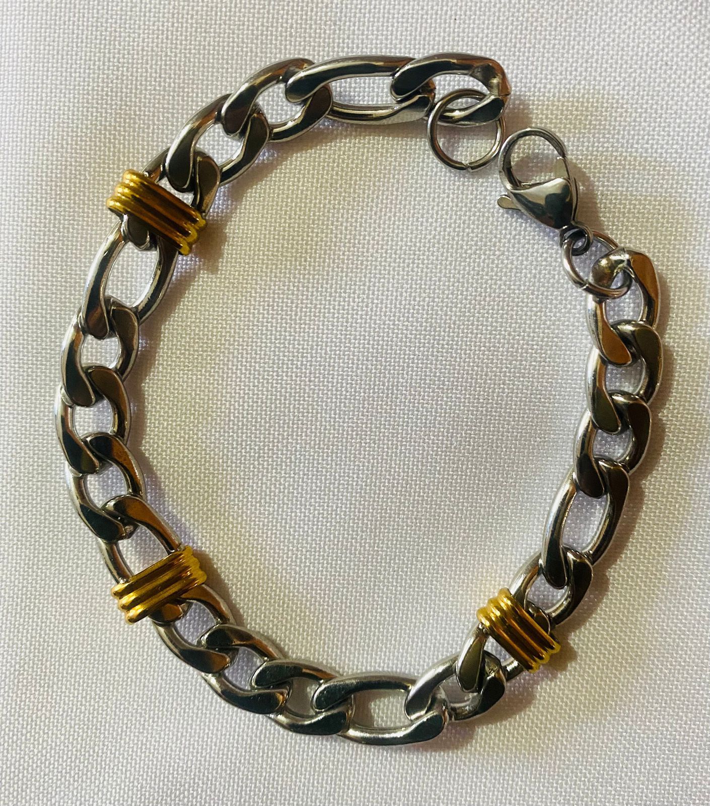 Una pulsera de plata y oro reposa sobre un paño blanco.